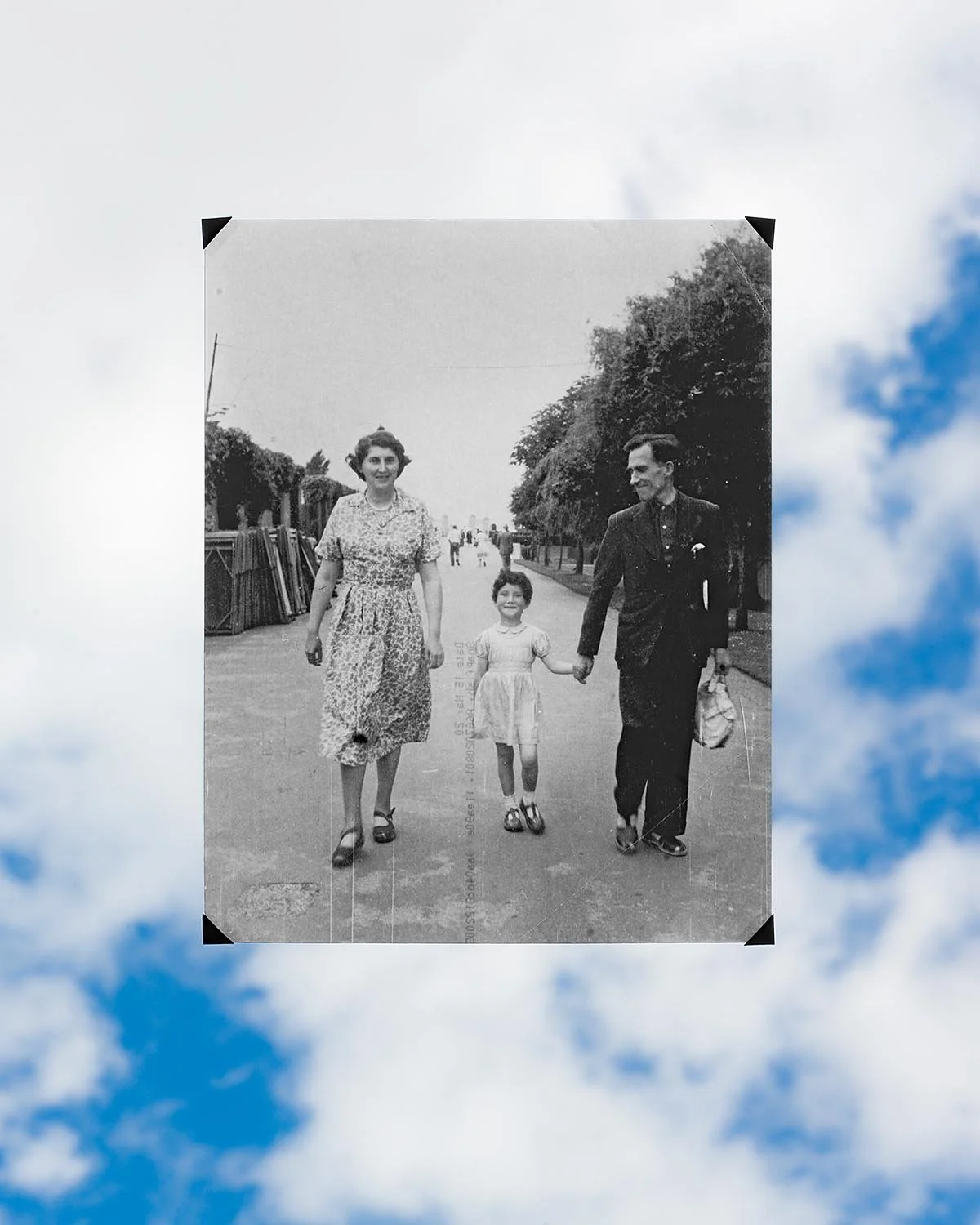 A vintage black and white photograph of a family walking outdoors on a street, holding hands and smiling.