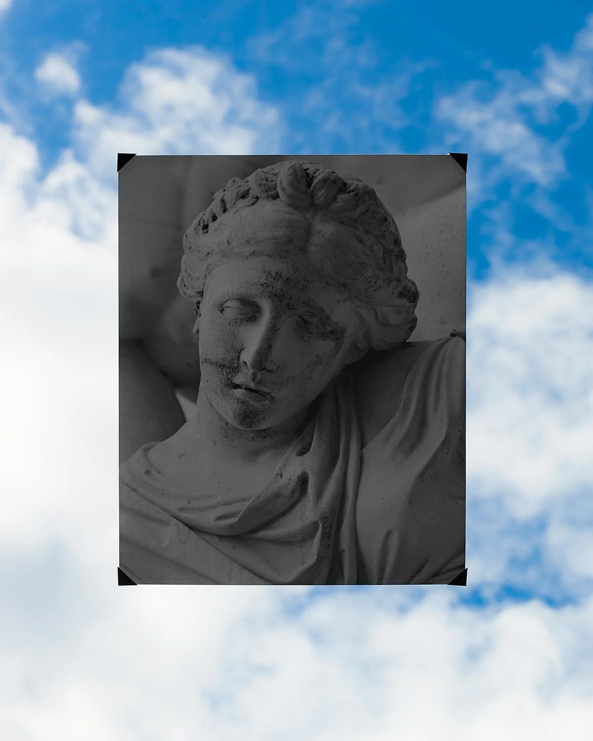 A grayscale bust sculpture of a woman with wavy hair, set against a cloudy blue sky.