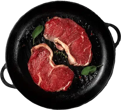 Two raw beef steaks seasoned with herbs in a black skillet