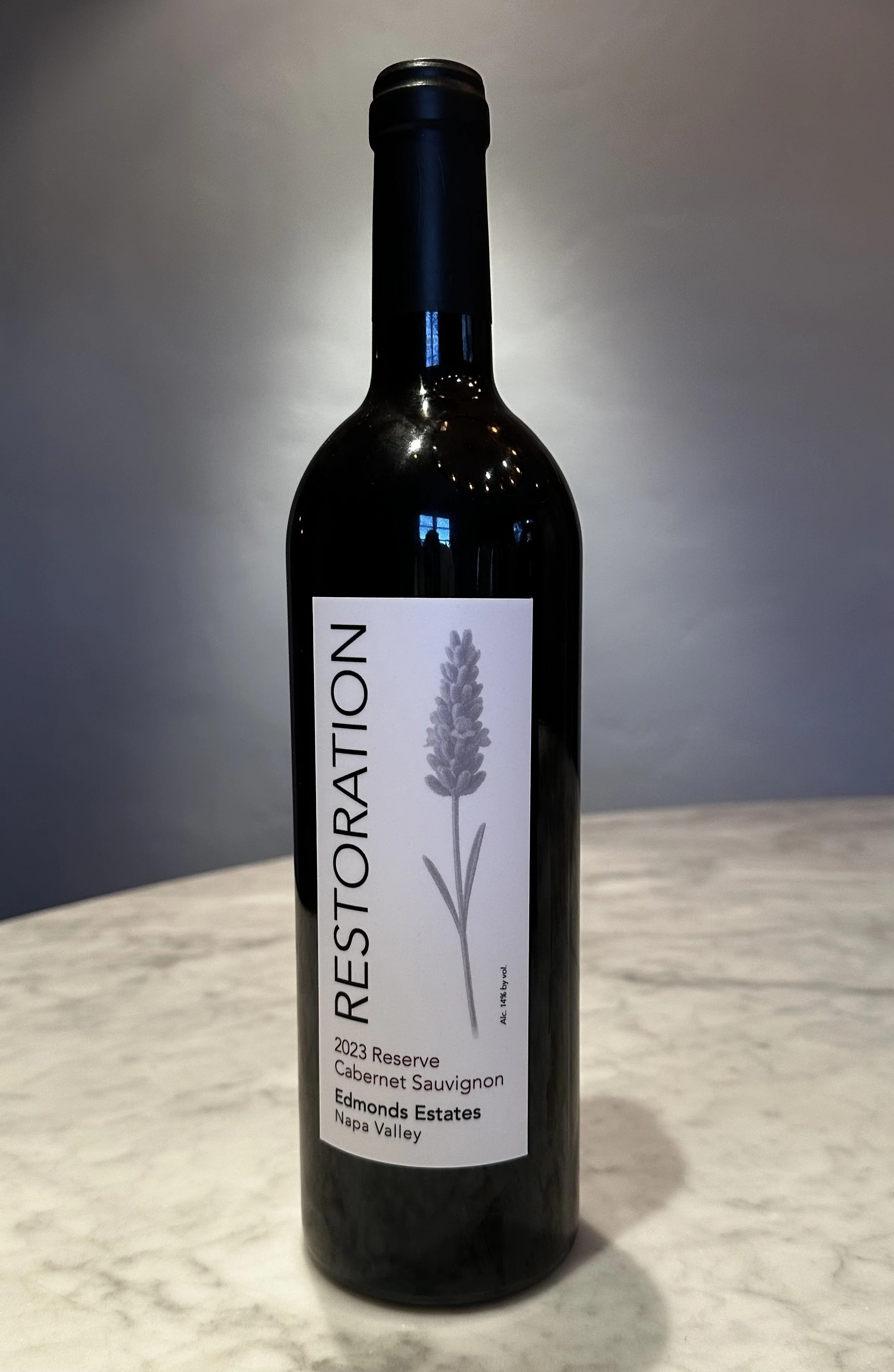 A bottle of red wine with a white label featuring a lavender illustration and the name 'Restoration' from Edmonds Estates, Napa Valley, 2023 Reserve Cabernet Sauvignon.