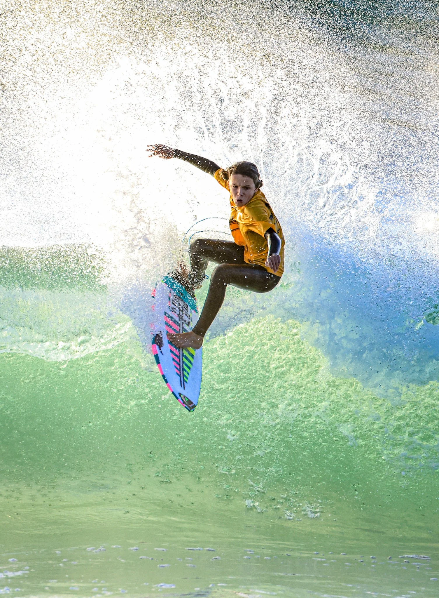 A person wakeboarding on a body of water, mid-air, with water splashing around them and wearing a yellow life jacket.