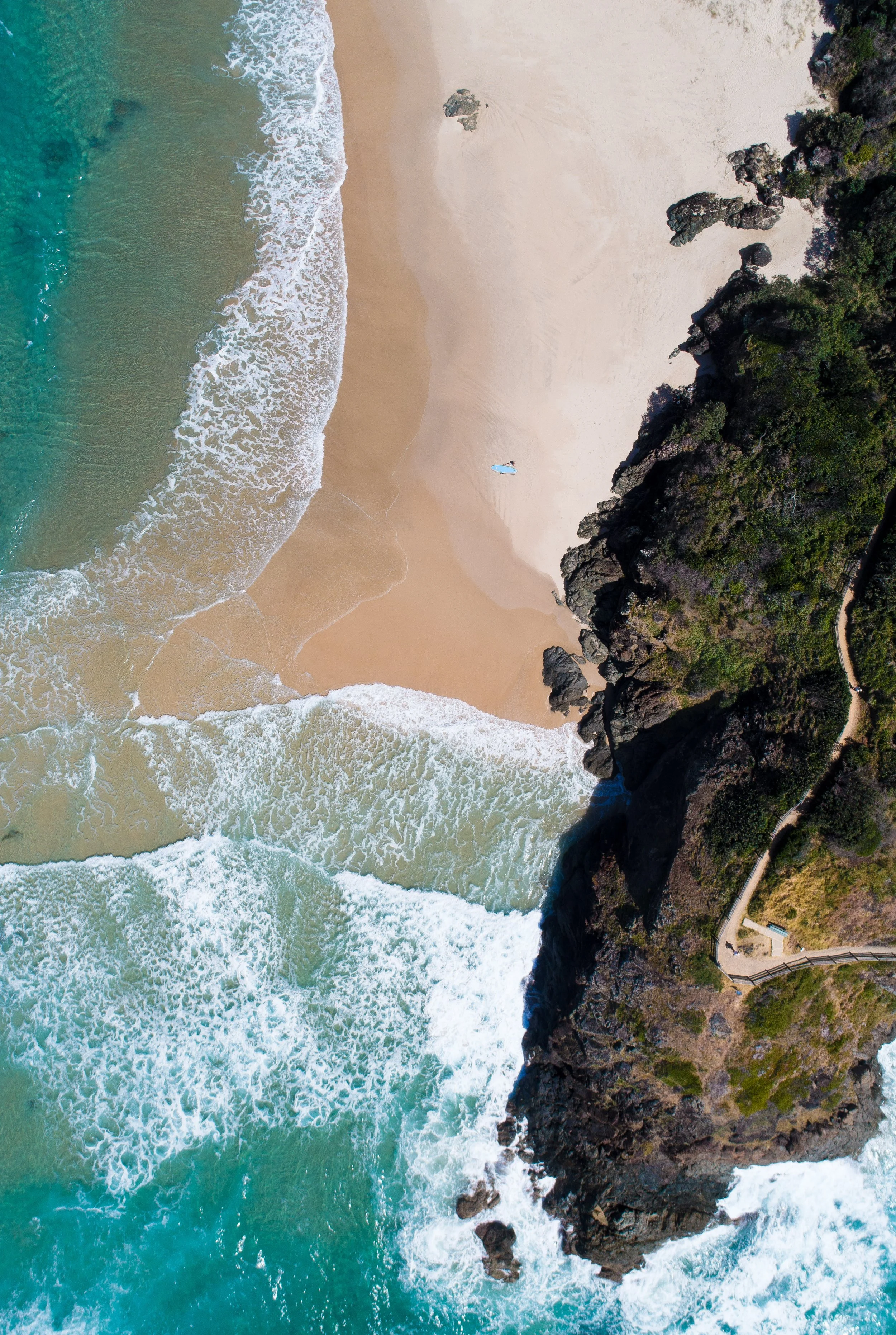 Aerial view of a beach with waves hitting the sandy shore and rocky cliffs covered in greenery.