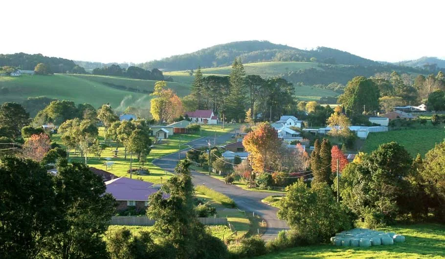 A scenic rural landscape with rolling green hills, scattered trees, houses, and a winding road.