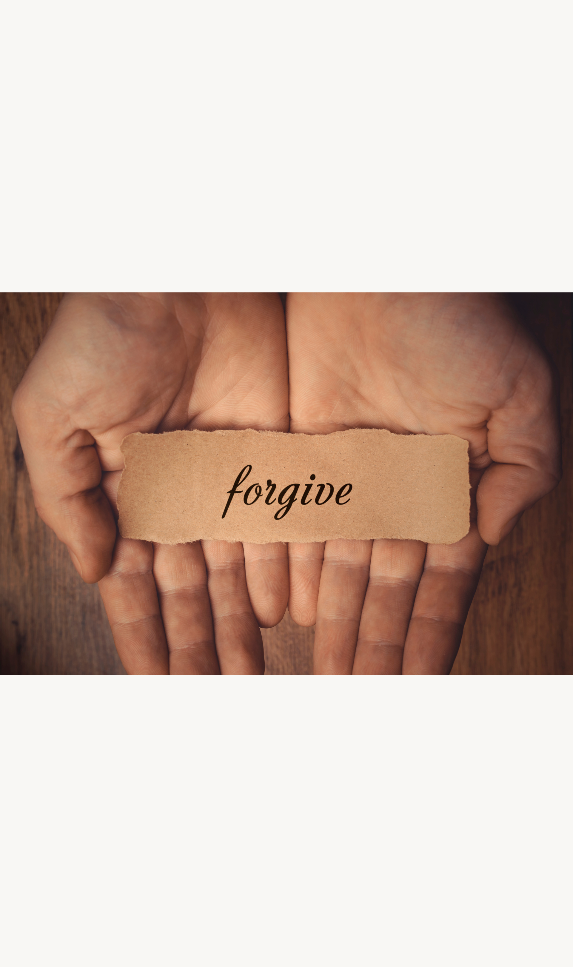 Two hands holding a torn piece of paper with the word 'forgive' written on it.