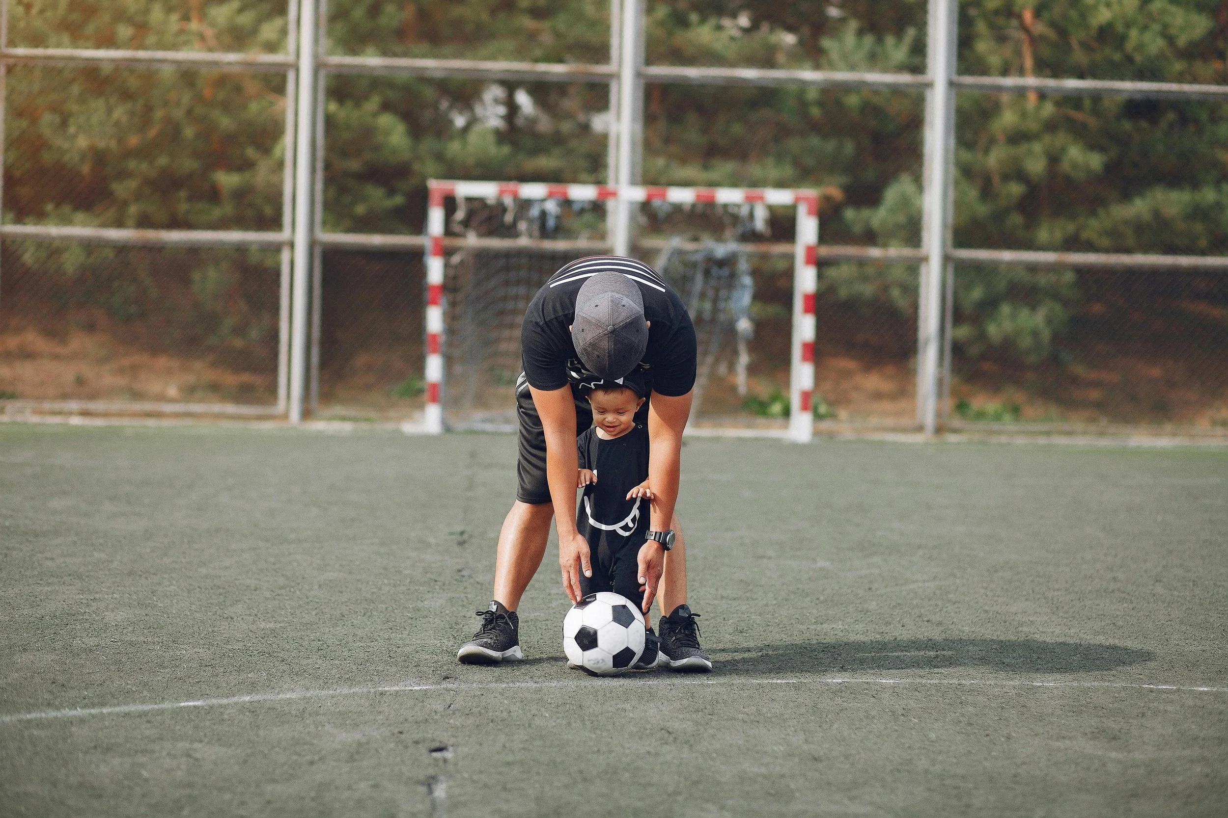 Adult and child preparing to kick a soccer ball on a field with goal in background
