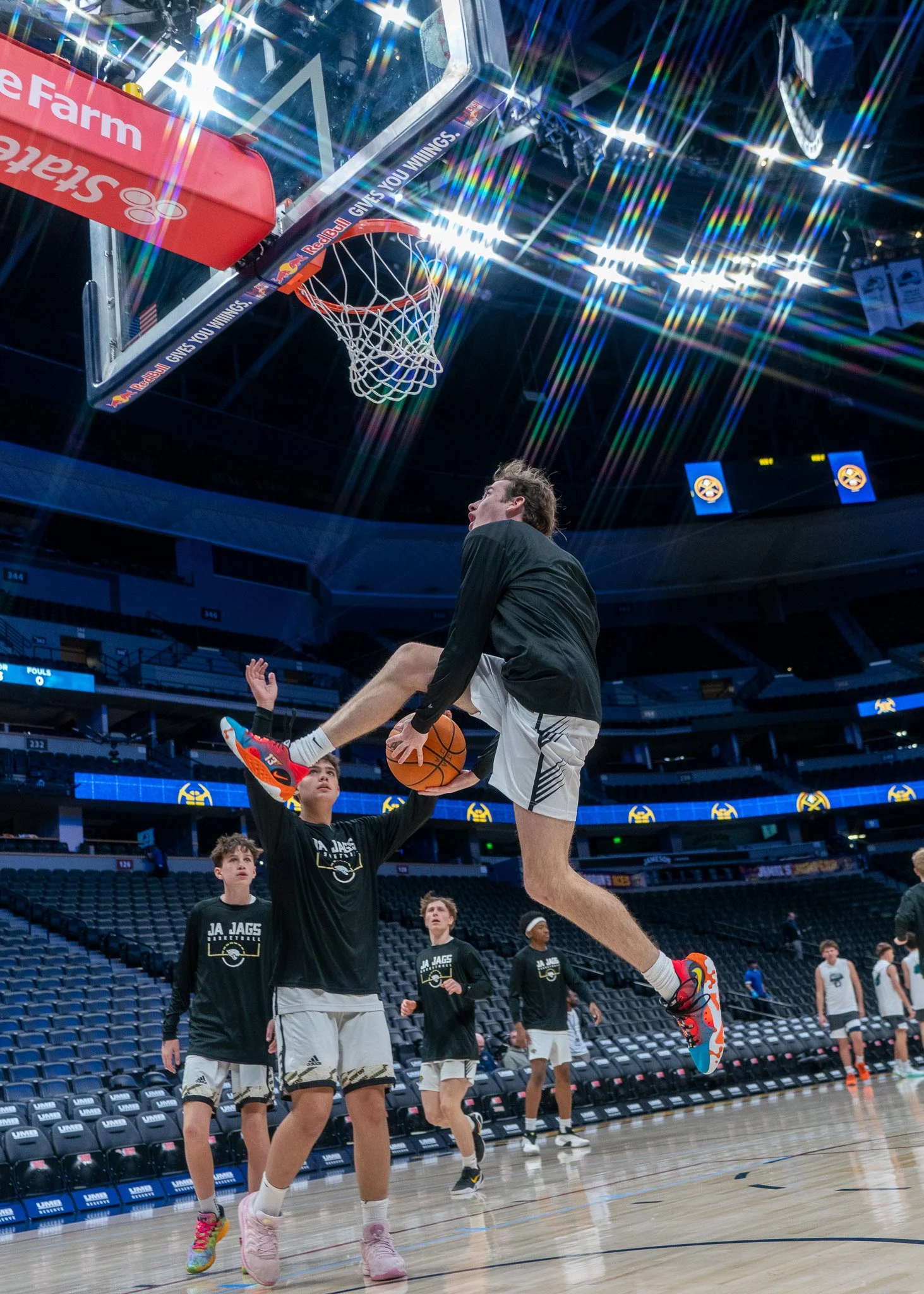 A male basketball player in a white jersey with the number 40 shooting a basketball in a gymnasium, with a scoreboard in the background and another player in the background.