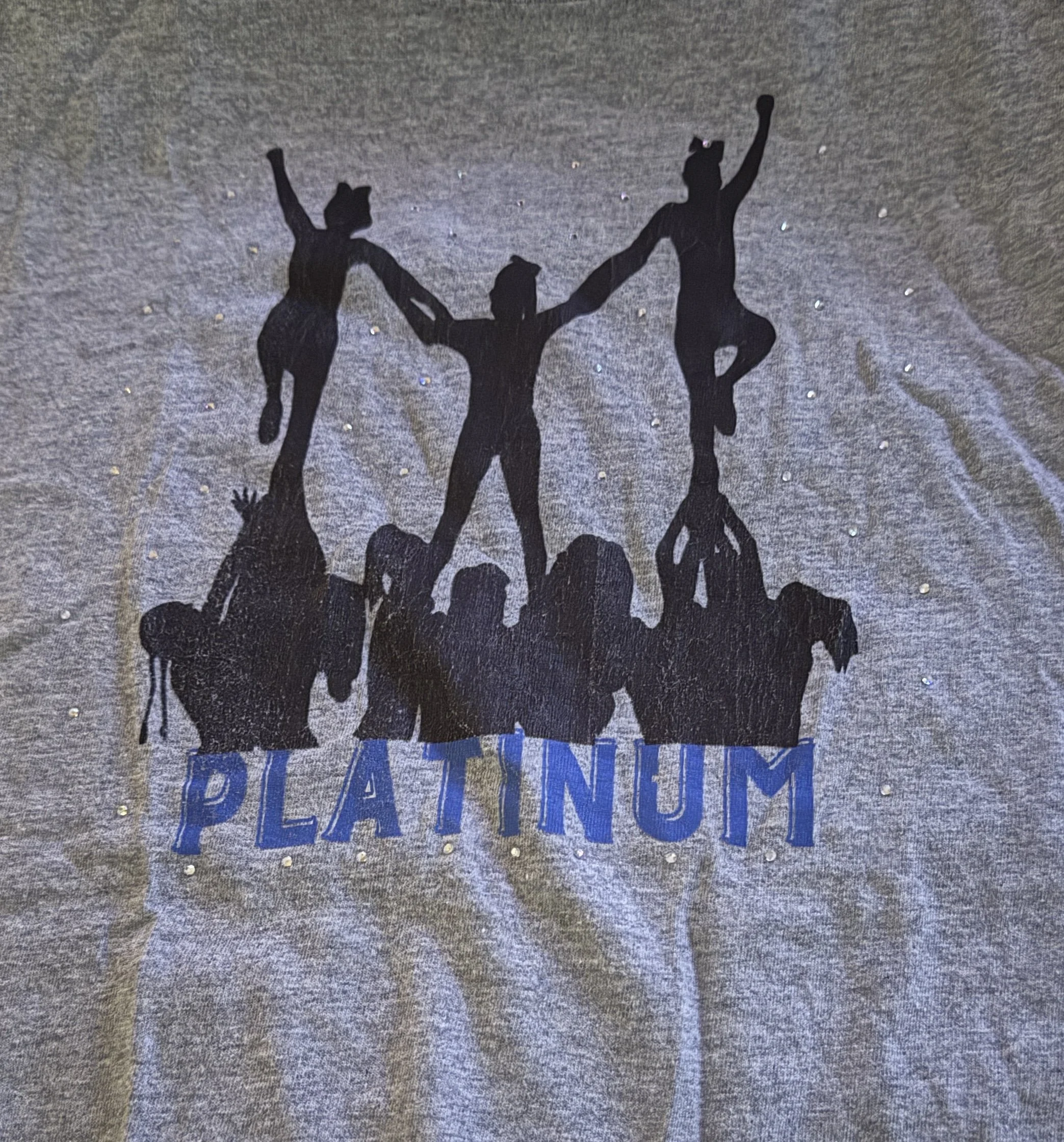 A graphic print on a gray T-shirt showing silhouettes of people forming a human pyramid with the word "PLATINUM" in blue underneath.