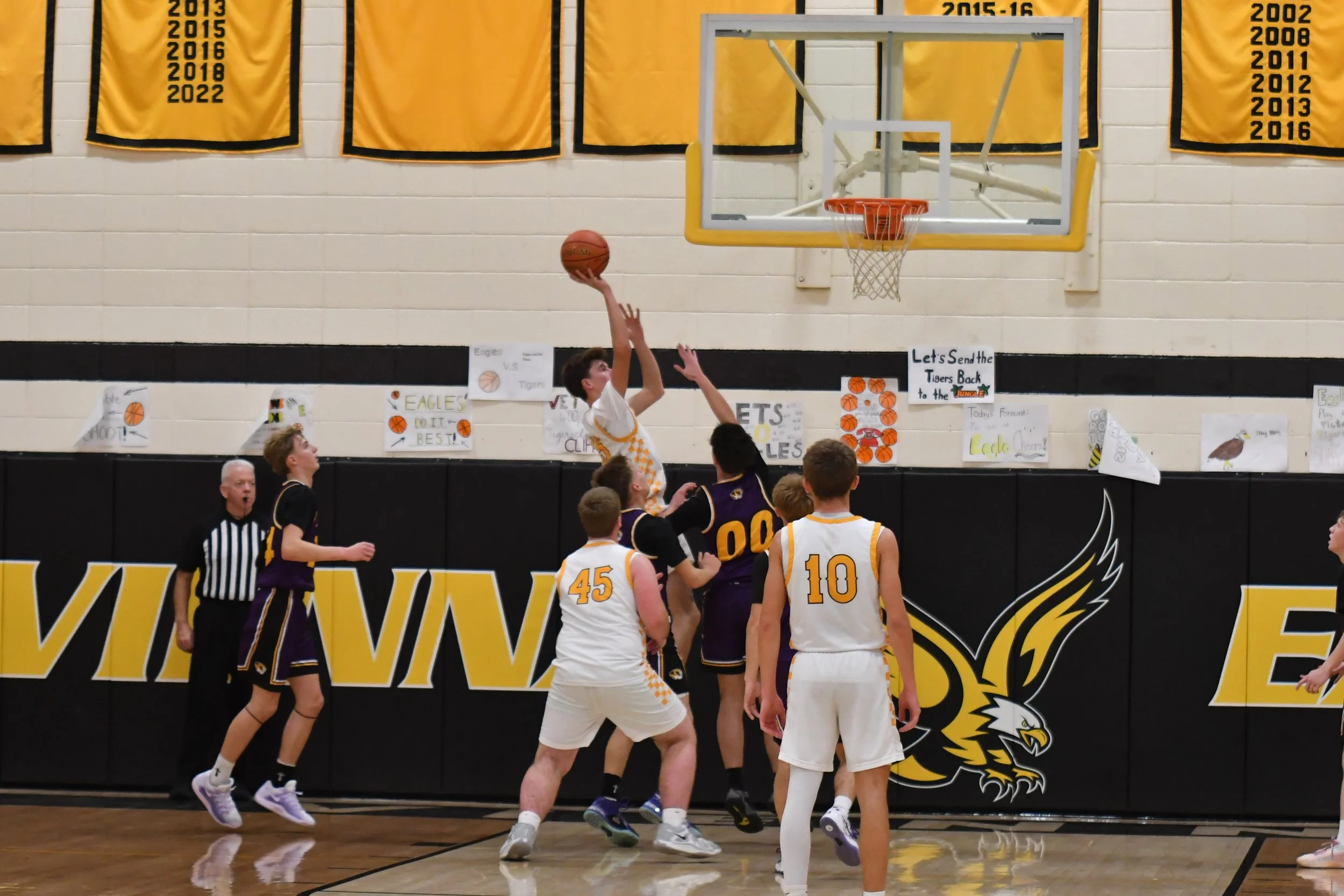 Young basketball players competing near the basket during a game in a school gym.
