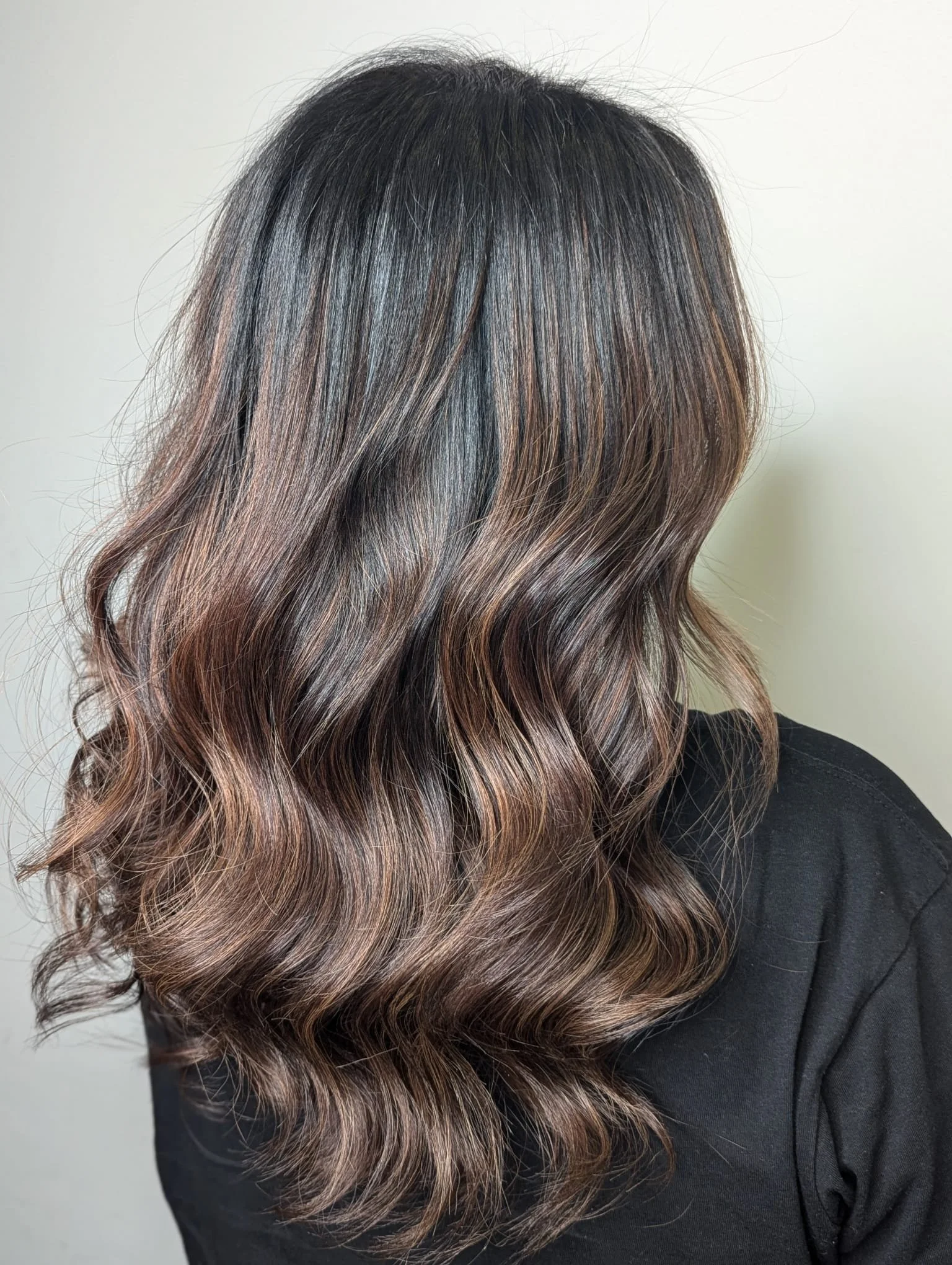 Back view of a woman with long, wavy hair showcasing a gradient from dark brown to lighter brown highlights.