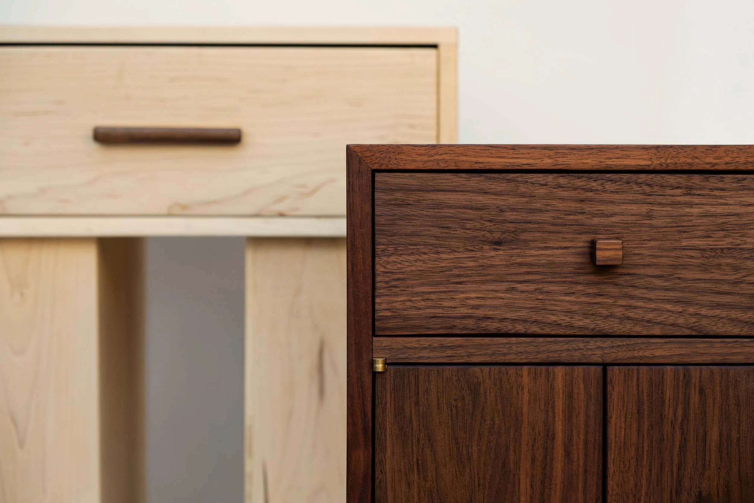 Close-up of two wooden cabinets, one dark stained and the other light stained, showcasing their drawers and handles.