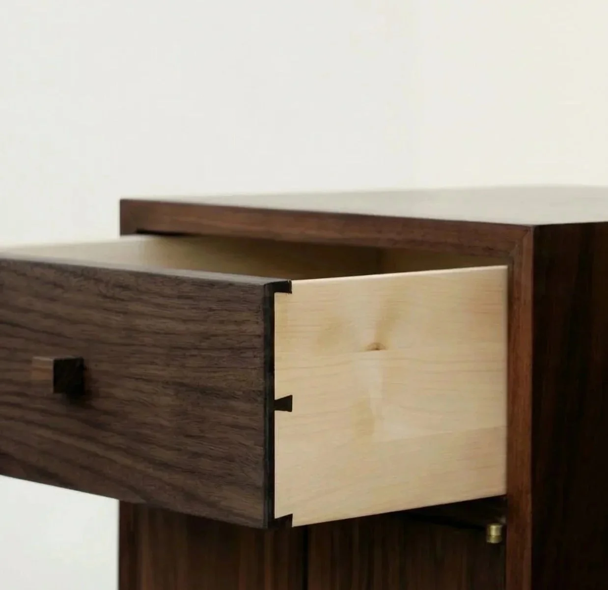 Close-up of a wooden drawer partially pulled open, showing a contrasting light wood interior and a dark wood exterior, on a wooden piece of furniture.