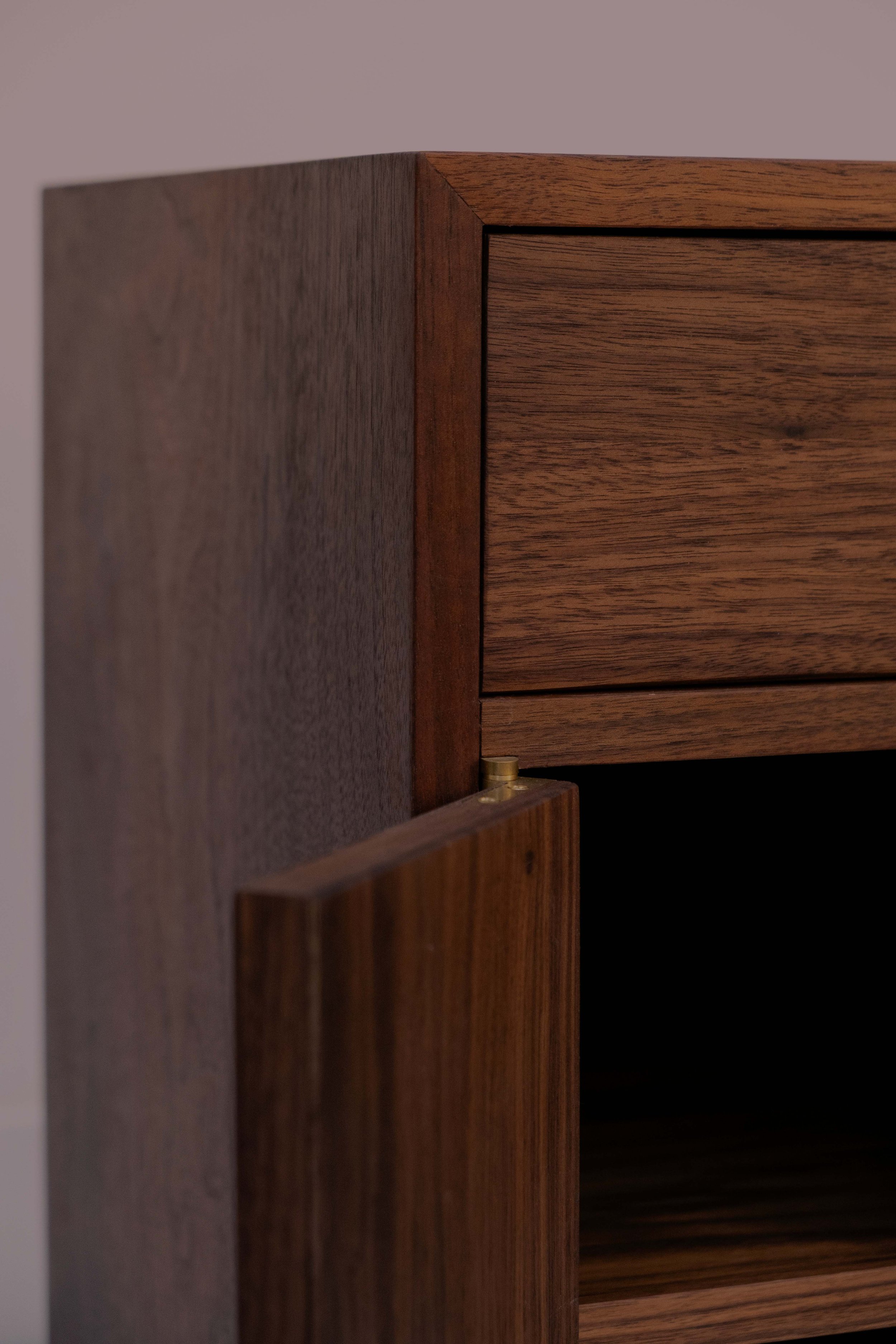 Close-up of a wooden cabinet with an open door, showing the wood grain and a brass hinge.