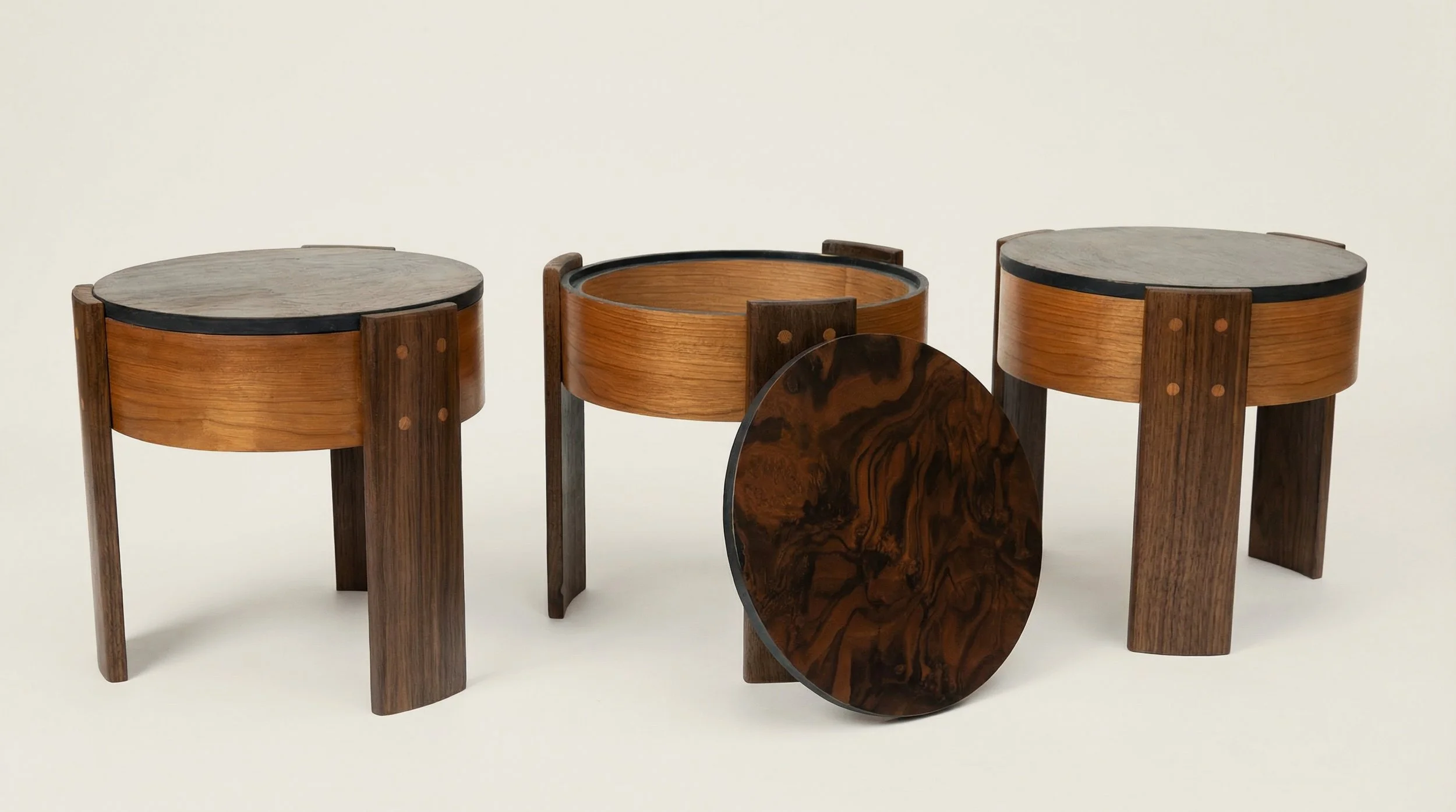 Three wooden stools with dark circular tops and a round decorative removable lid leaning against the center table.