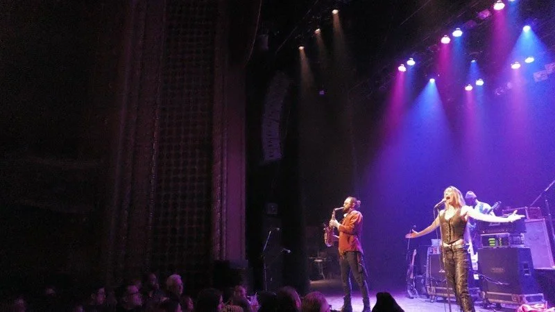 Musicians performing on stage with colorful lights and a crowd watching.