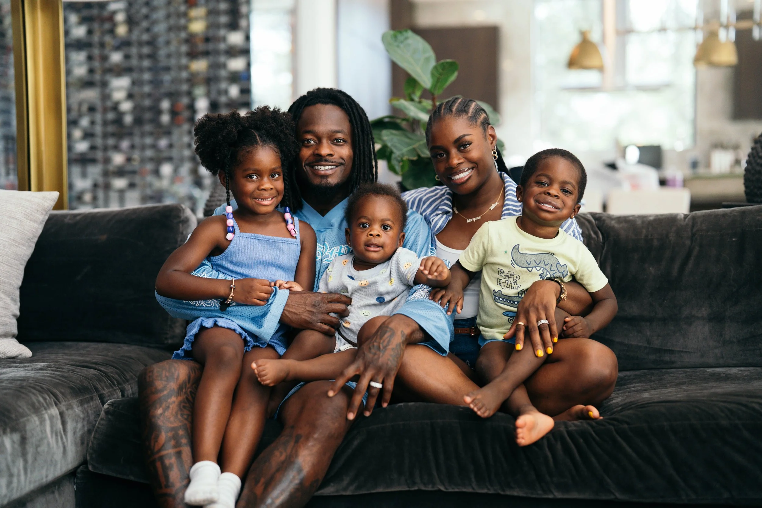 A happy family of five sitting on a dark grey couch in a bright living room.