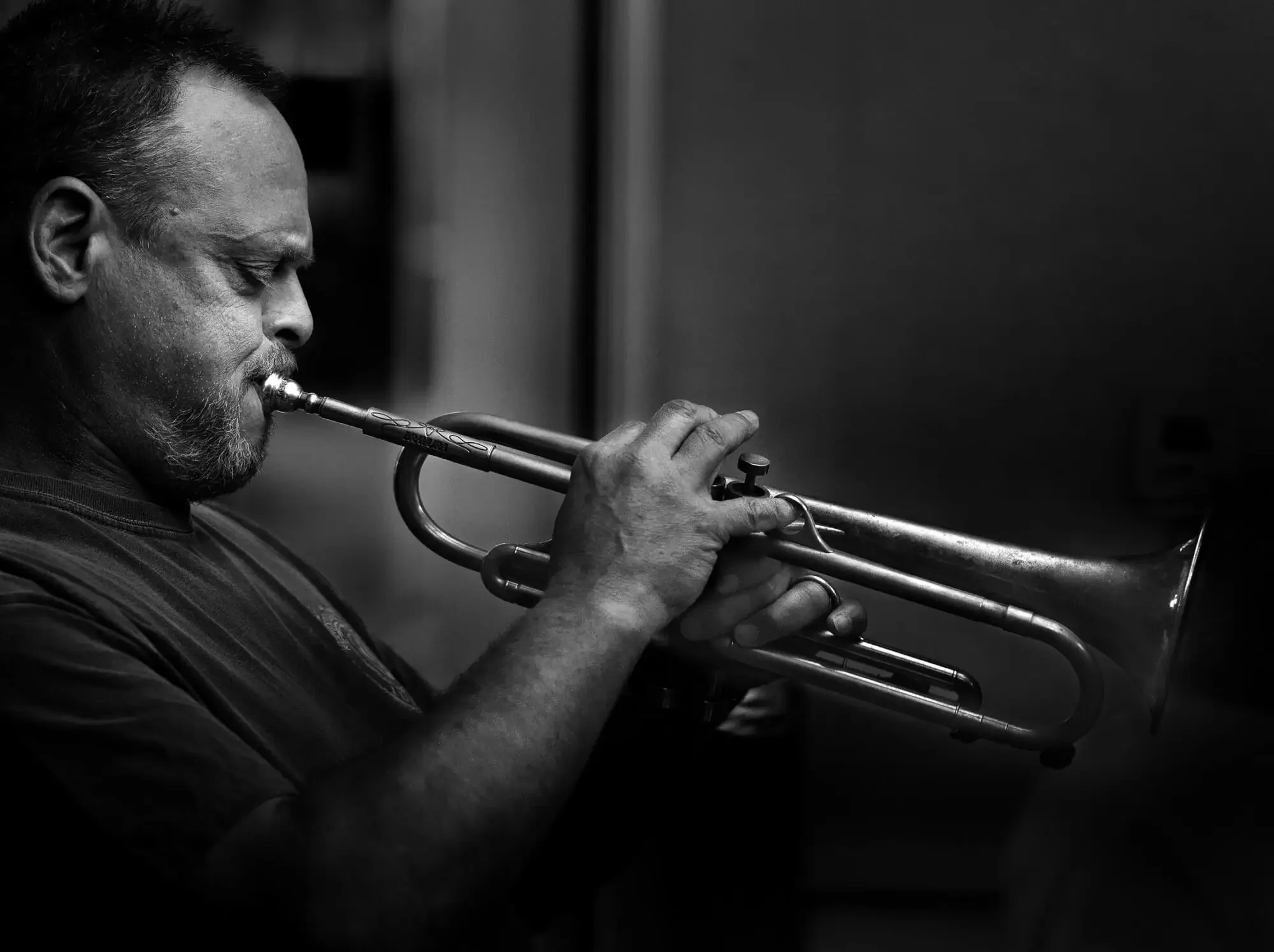 A man playing the trumpet, with his eyes closed, in a black and white photograph.