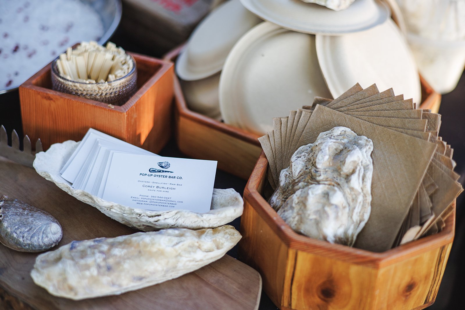 A display of oyster shells, business cards from Pop-Up Oyster Bar Co., and paper napkins in wooden boxes at a seafood market or event.