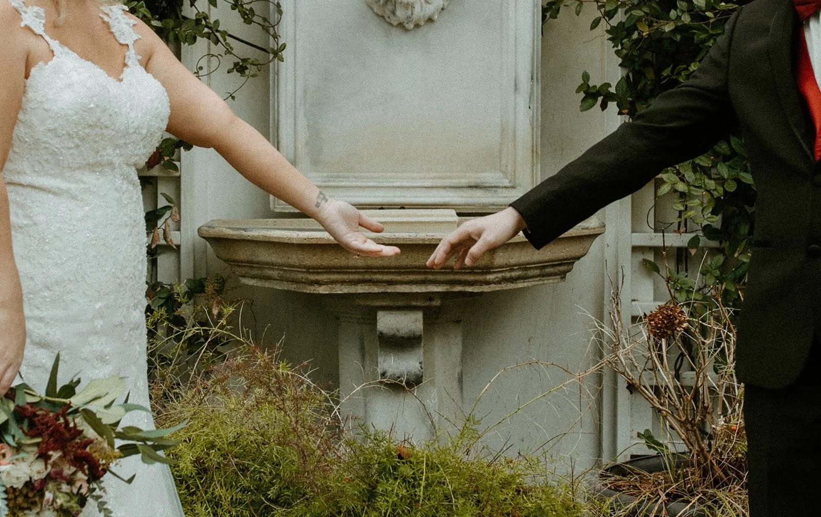 A bride and groom reaching out to touch hands during their wedding ceremony outdoors.