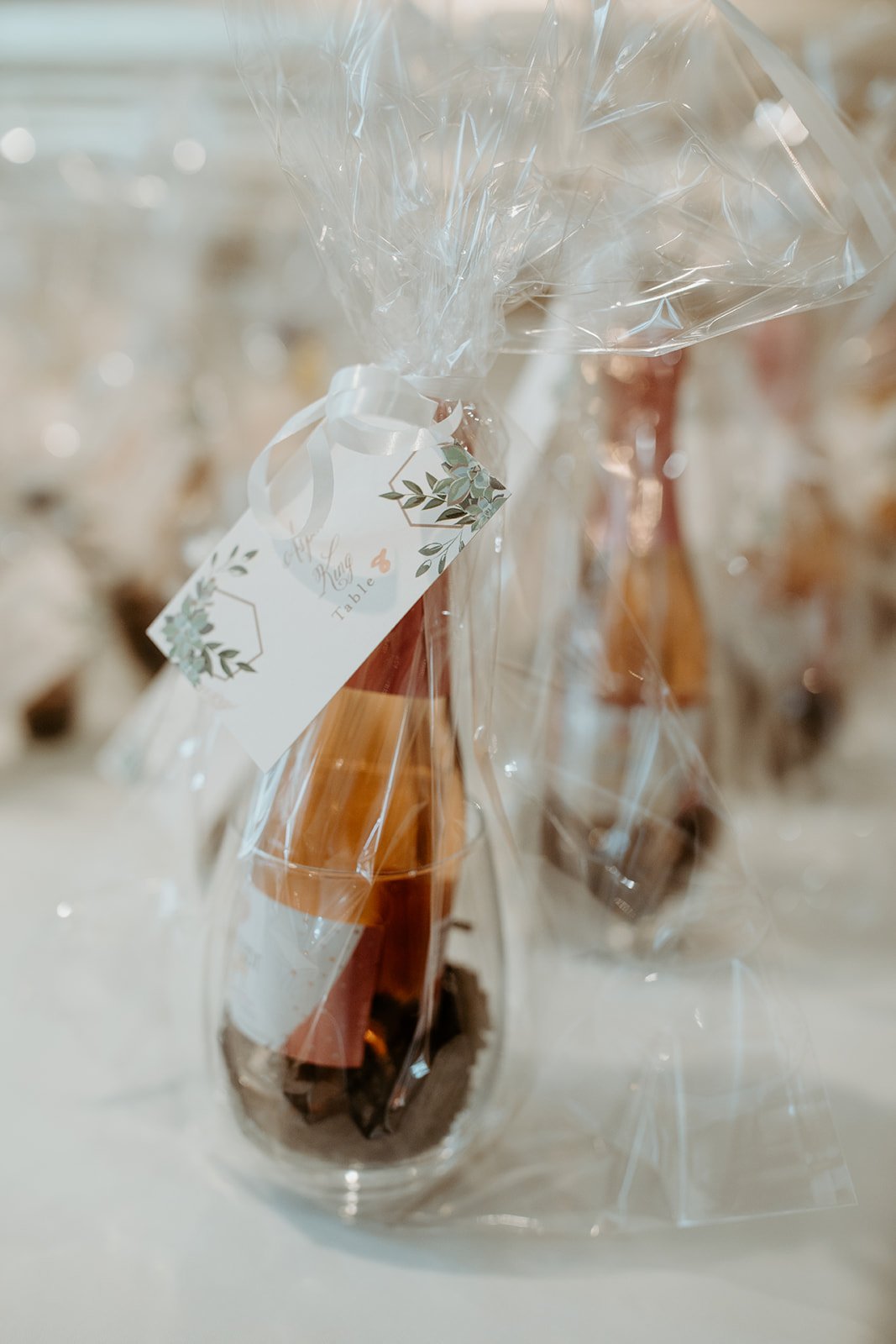 Glass bottles wrapped in plastic, with a label that reads 'Table 4', decorated with green leaves, at a celebration or wedding event.