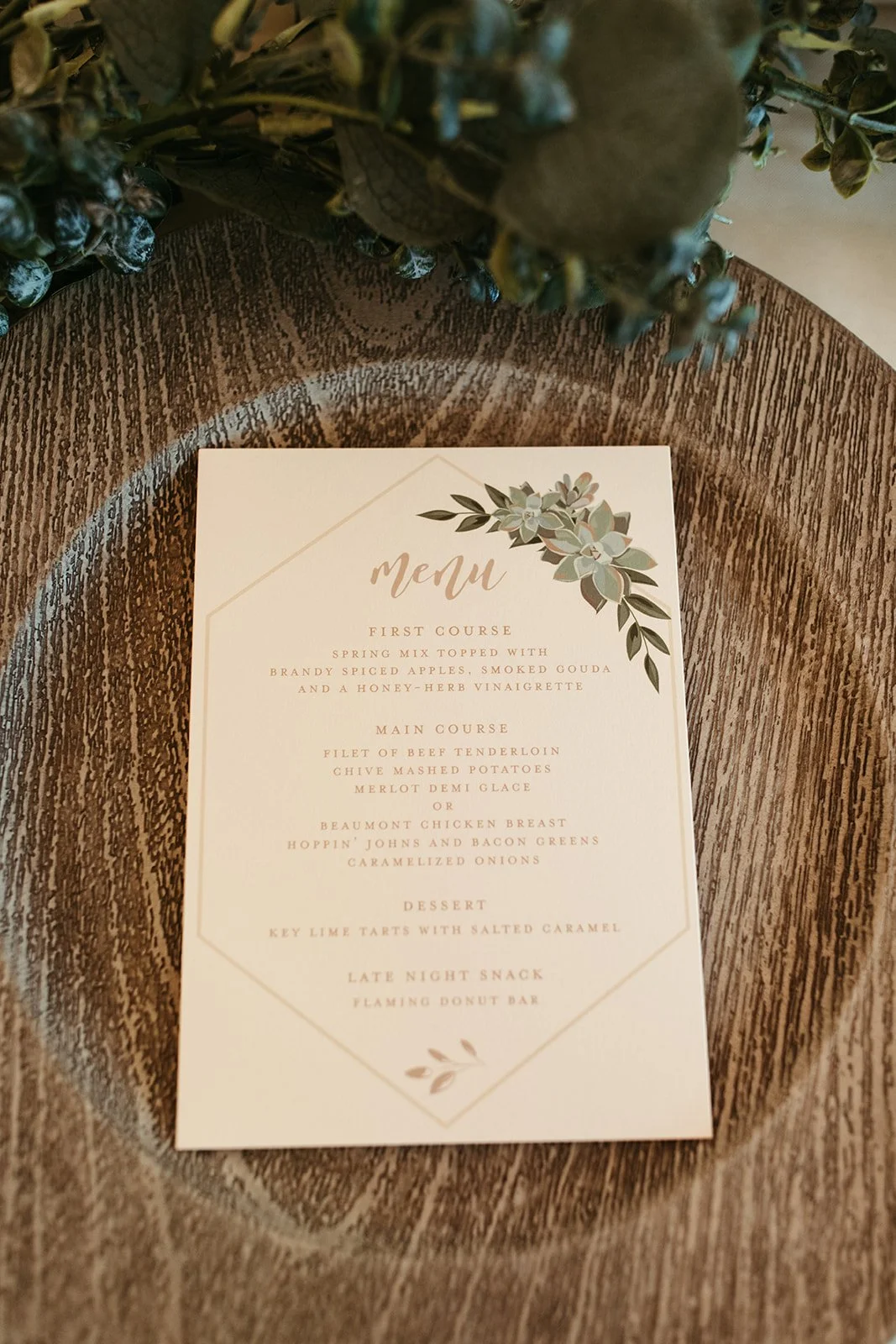 A menu card placed on a wooden surface with green leafy decoration at the top. The menu lists courses including first course, main course, dessert, and late night snack, with various dishes.