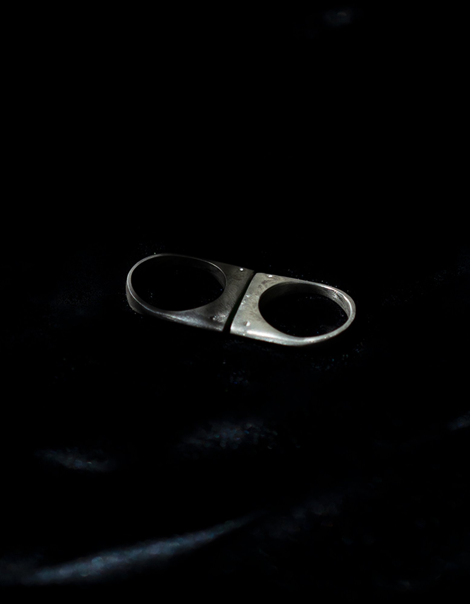 A silver, metallic, double-sided fidget toy with holes, placed on a dark, shadowed surface.