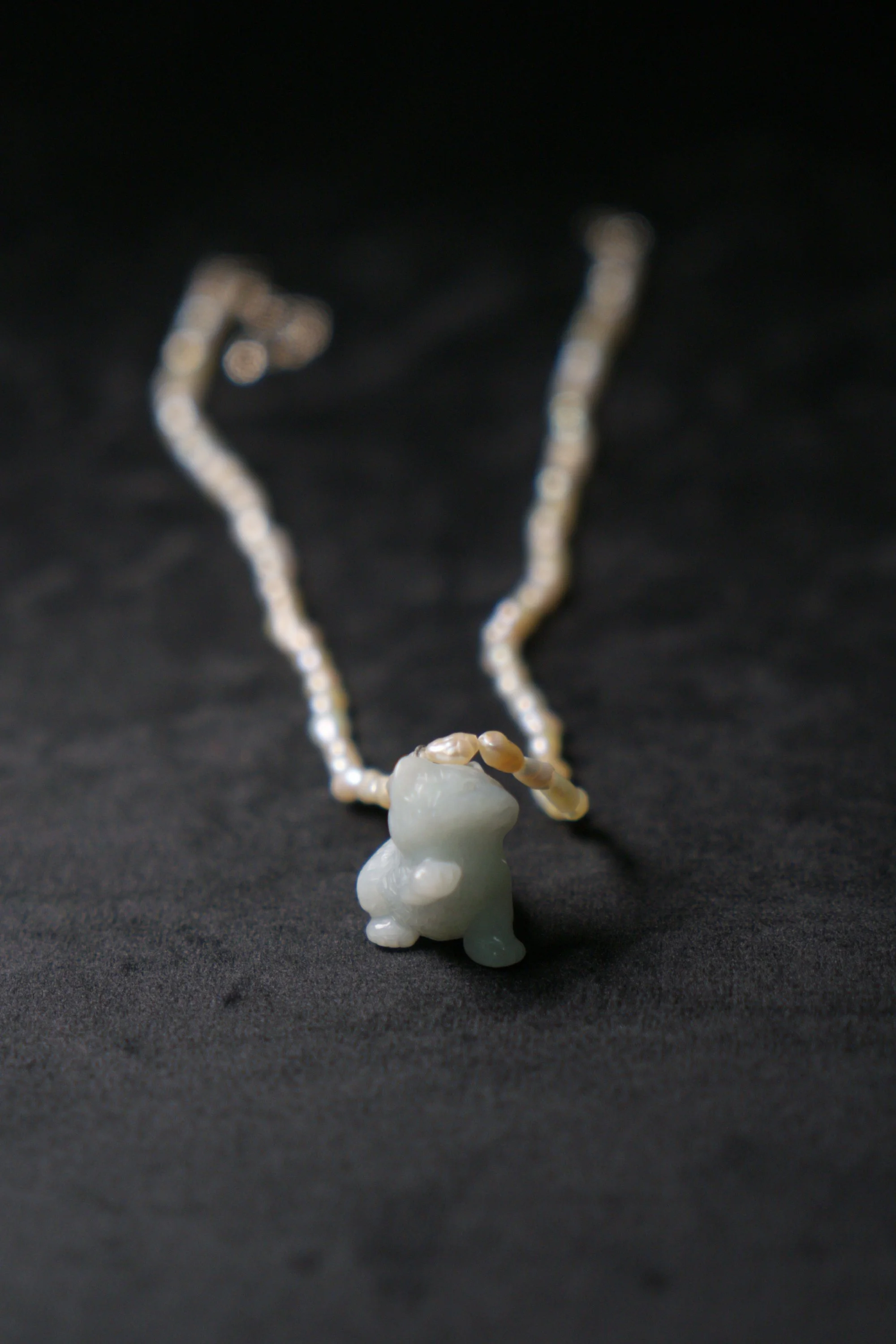 A white jade frog pendant with pearl and beige bead necklace on black fabric background.