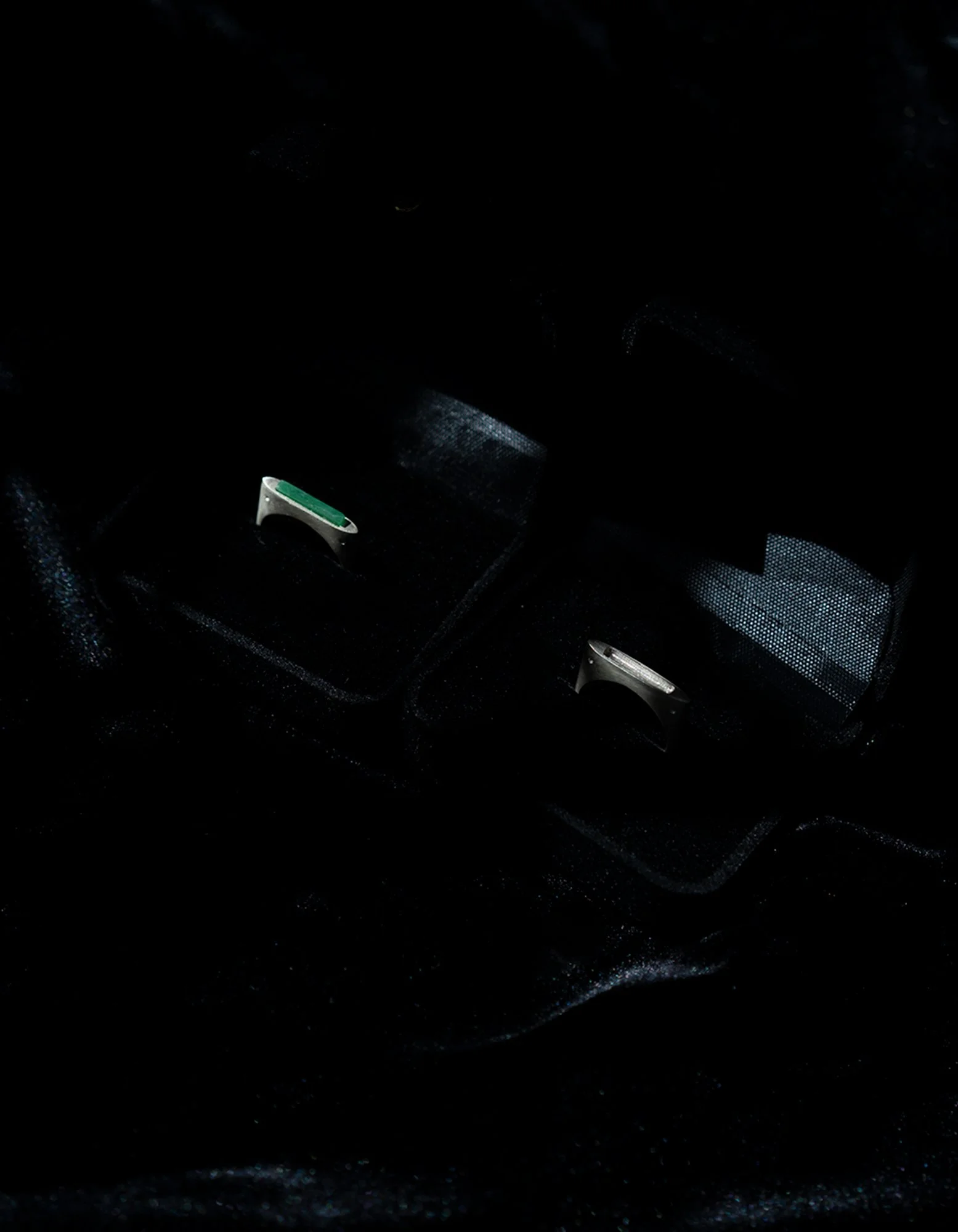 Two rings, one with a green accent, placed in open black velvet jewelry boxes.