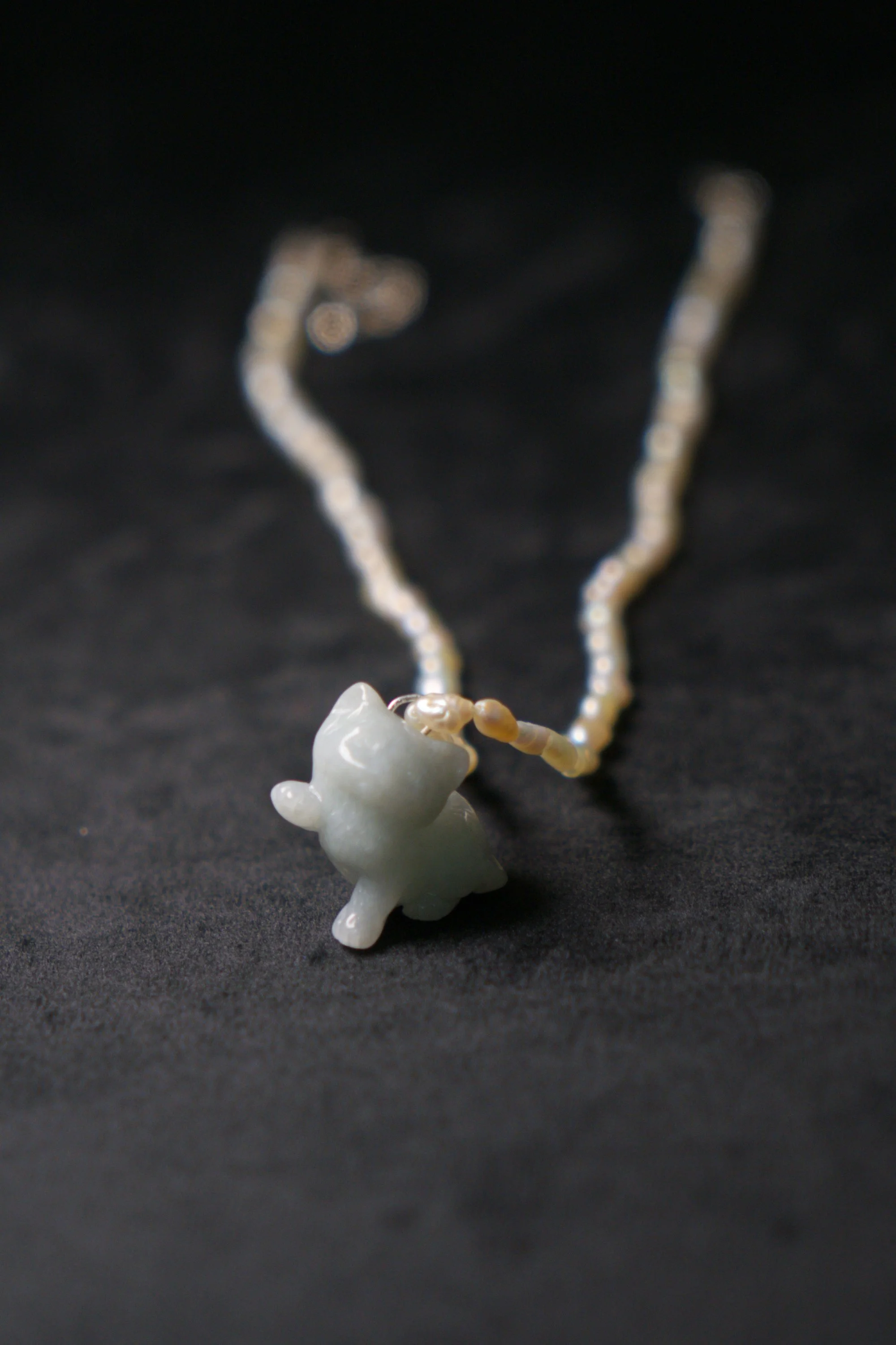 A necklace with a pendant shaped like a small animal, possibly a pig or a similar creature, lying on a black surface.