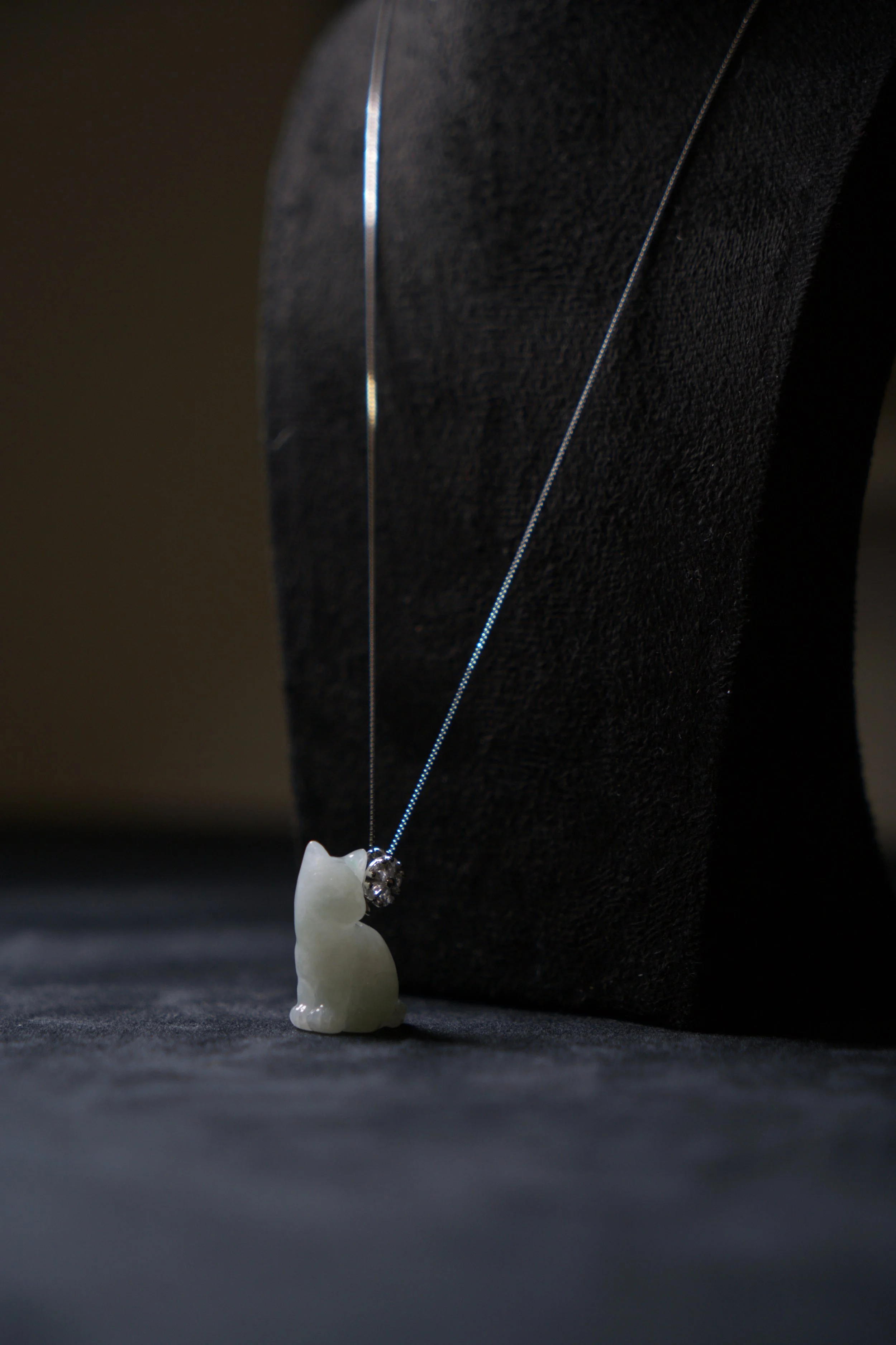 Pendant necklace with a small cat-shaped carved white jade or stone figure, displayed on a jewelry stand.