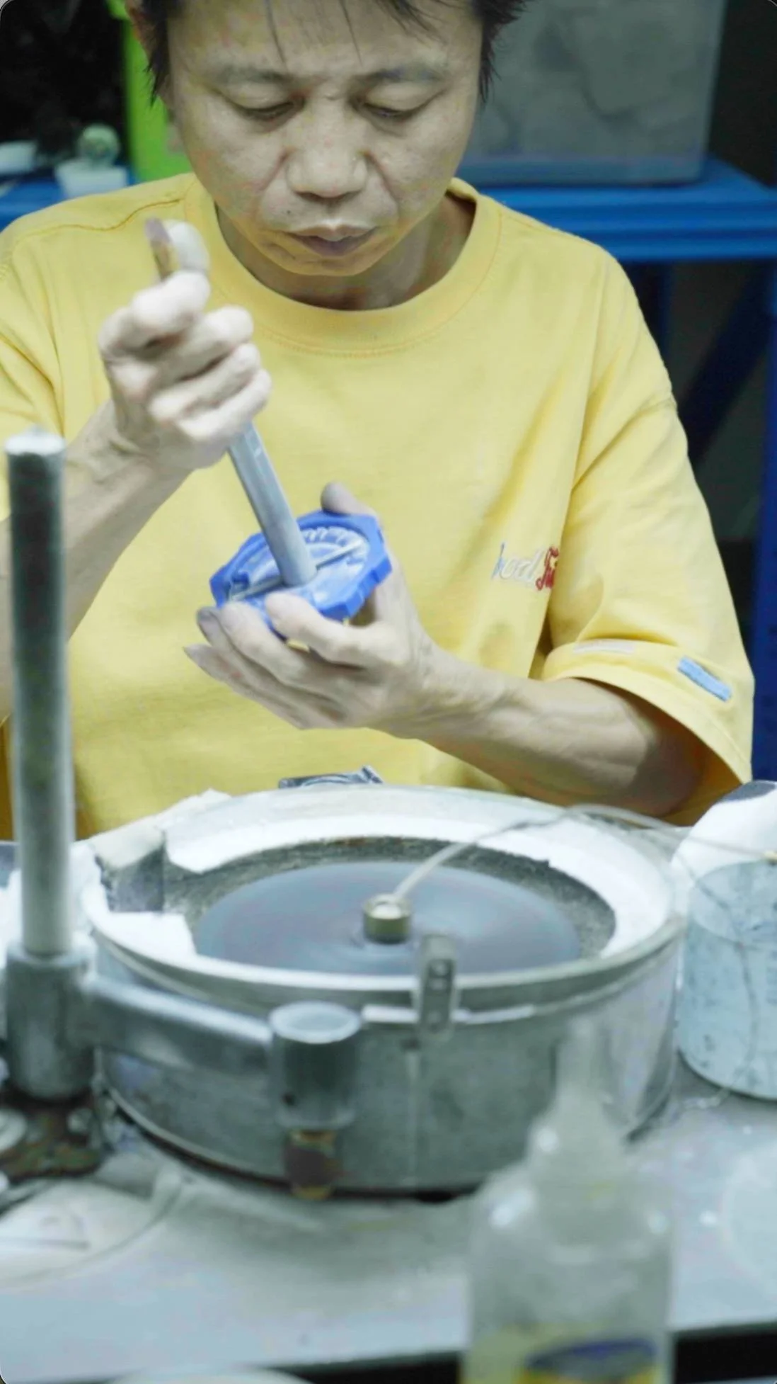A man in a yellow shirt working with a mold in a laboratory or manufacturing setting, apparently handling a component of a device or product.