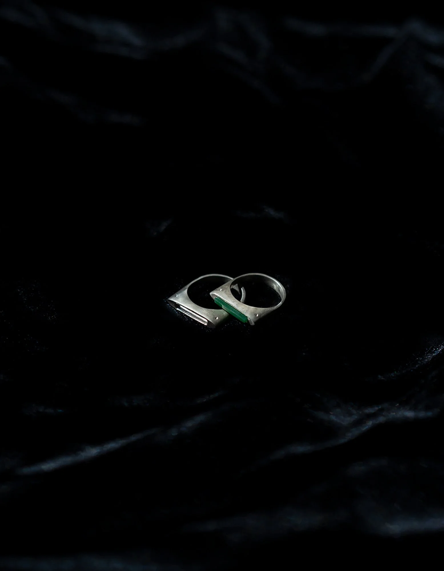 A close-up of a silver ring and a silver bracelet placed on black fabric.