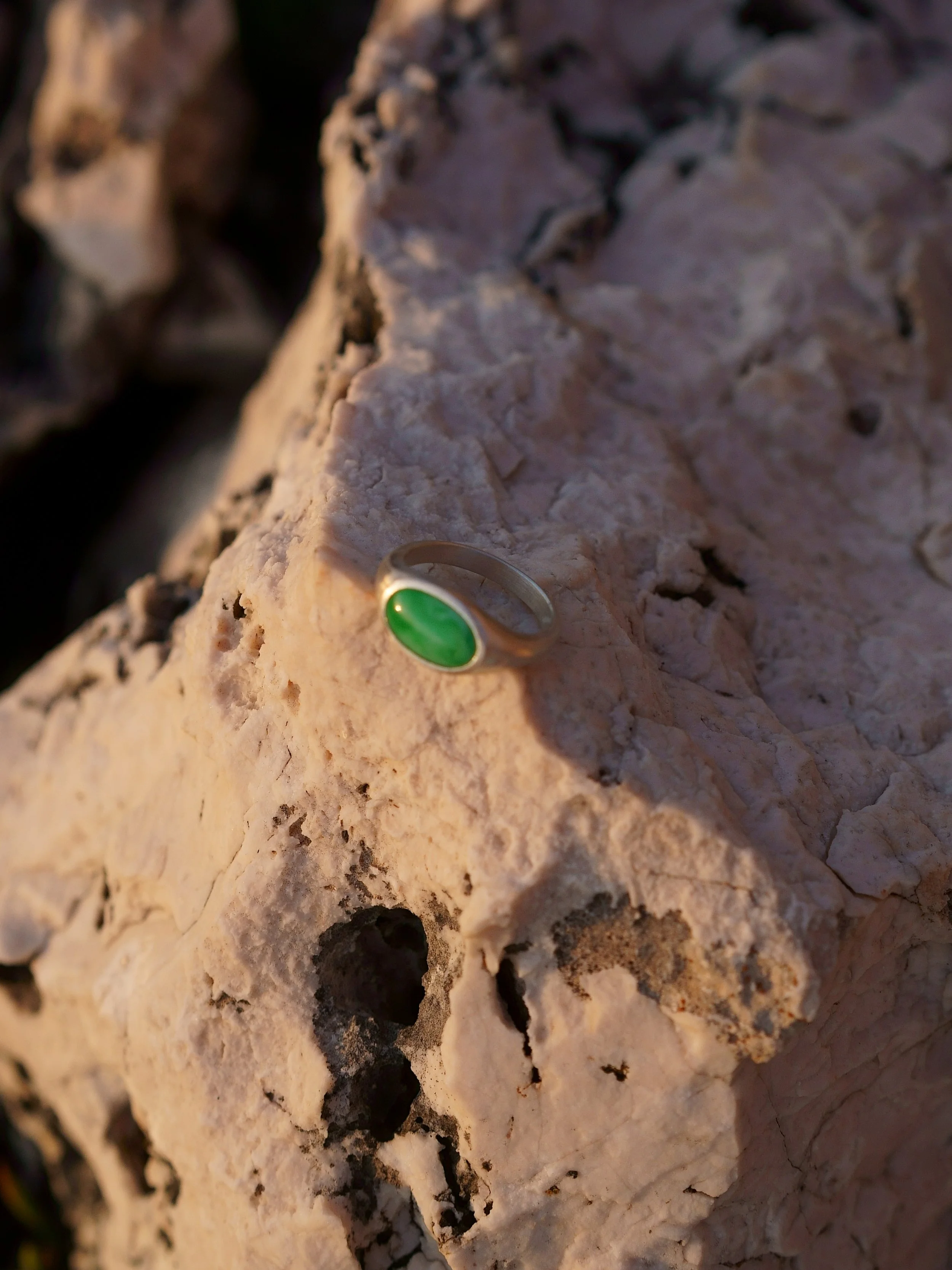 A silver ring with a green oval stone resting on a large, textured rock.