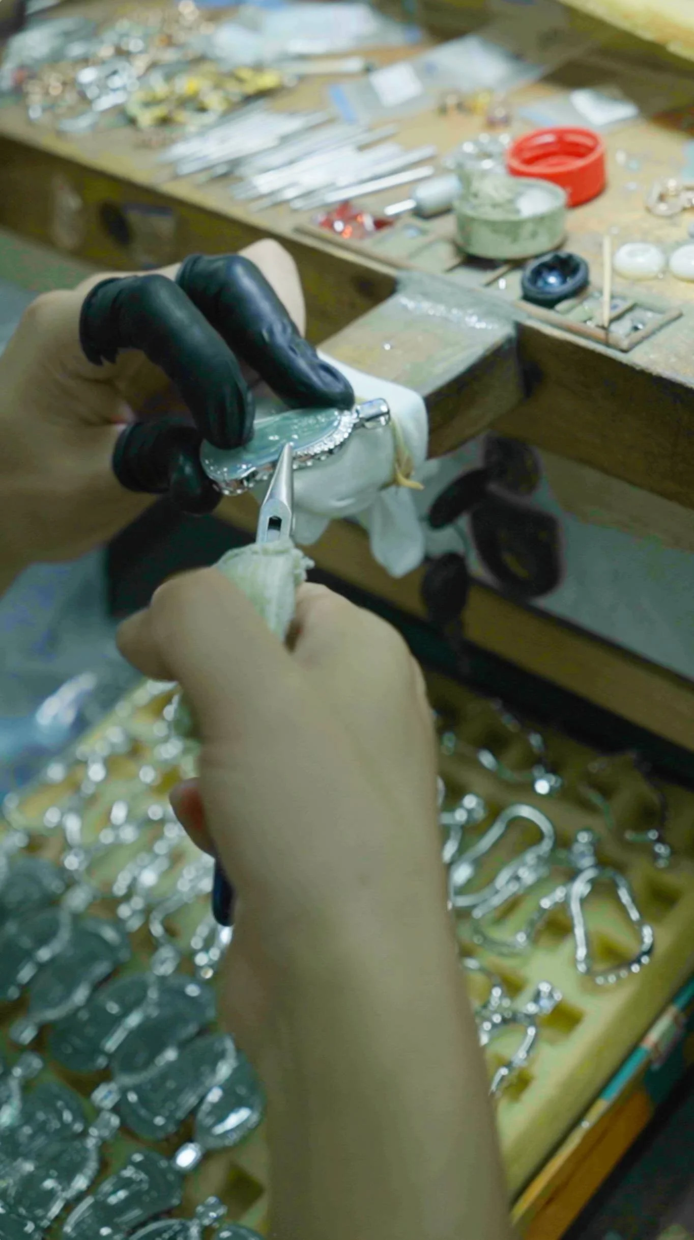 Jeweler crafting a silver bracelet on a workbench with jewelry tools and parts.