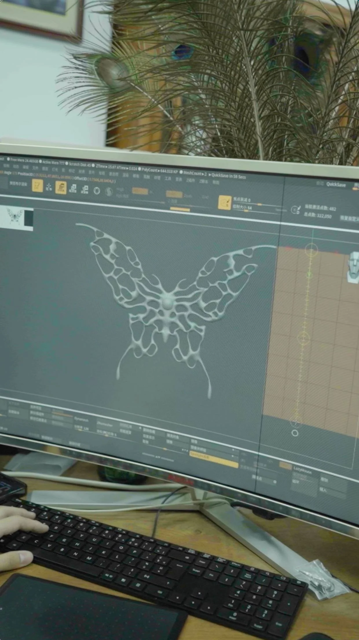 Computer monitor displaying 3D butterfly design, along with a keyboard and a person's hand on the keyboard at a desk.