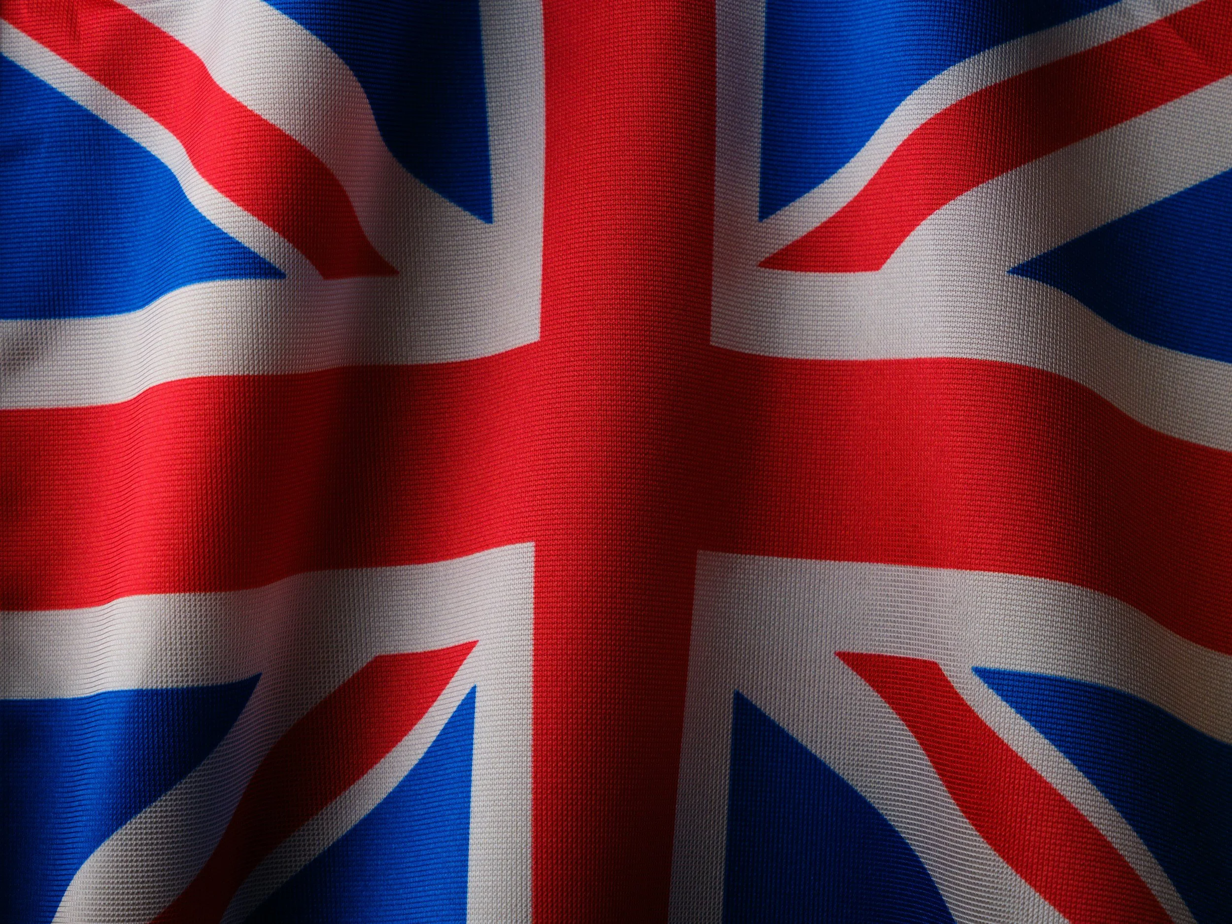 A close-up view of the United Kingdom flag, also known as the Union Jack, showing its red, white, and blue design with a folded fabric texture.