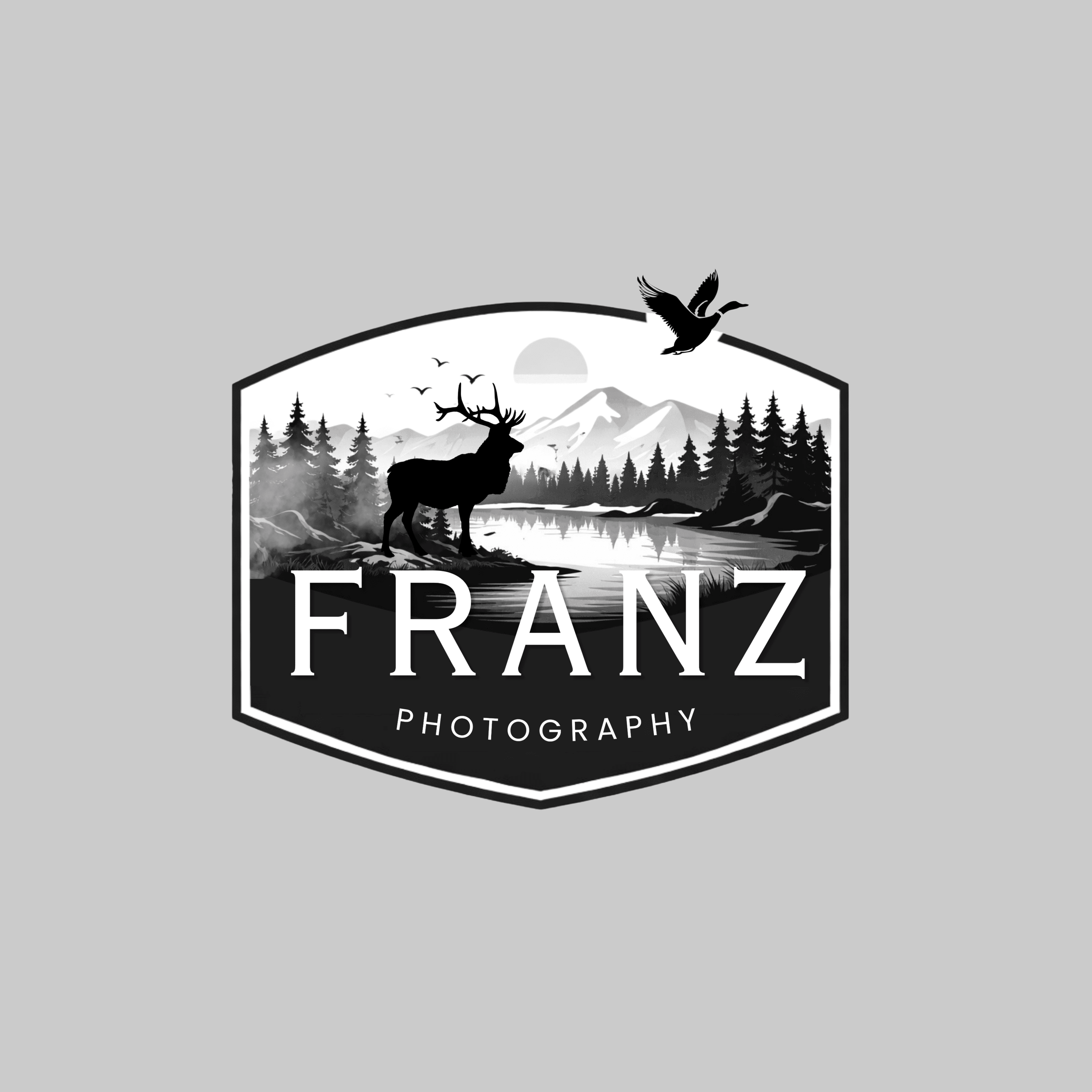 A black and white logo for Franz Photography featuring a nature scene with a deer, trees, mountains, a lake, and flying birds.