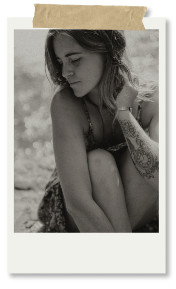 A young woman with tattoos, sitting outdoors with her eyes closed, in black and white.