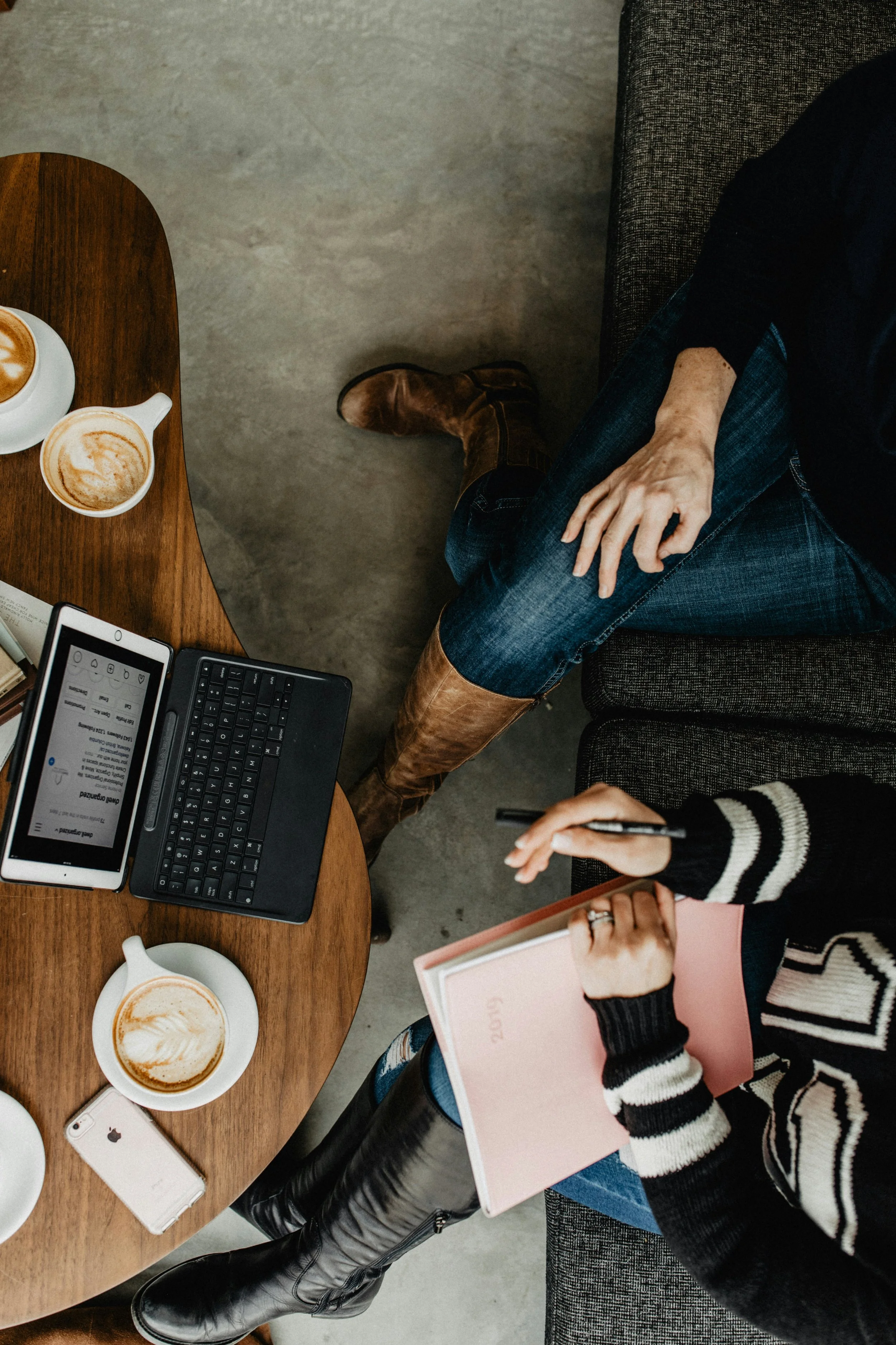 Two women are talking on a couch with a laptop and two coffees on the table in front of them.