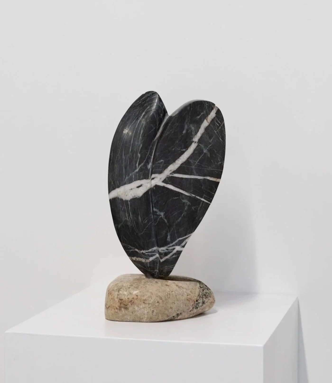 A black marble sculpture shaped like a broken heart, mounted on a light-colored stone base, set against a plain white background.