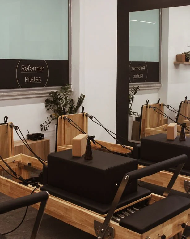Pilates reformer machines in a fitness studio with a wall mirror and a plant.