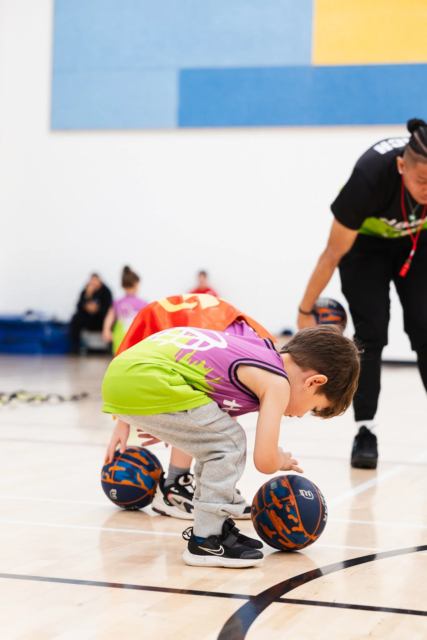 Young boy squatting on a basketball court, dribbling a basketball during a basketball training session.