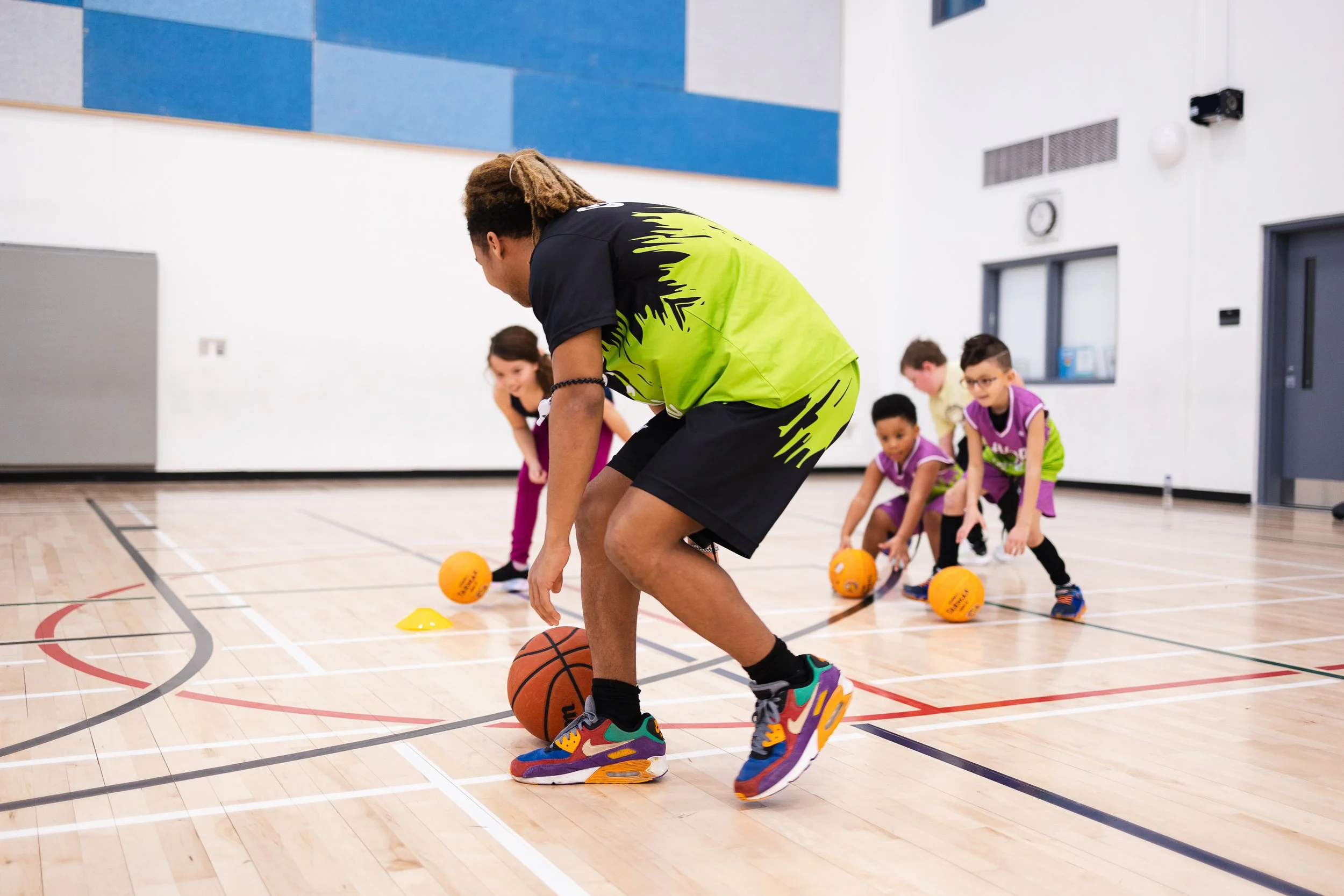 Kids learning basketball dribbling skills from coach in gym.