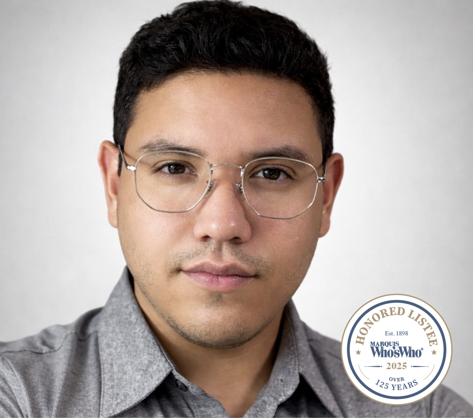 Close-up photo of a young man with dark hair, wearing glasses and a gray collared shirt. There is what appears to be a valid badge or seal in the lower right corner that reads 'Honored Lister, Marquis Who's Who, since 1898, over 125 years.'