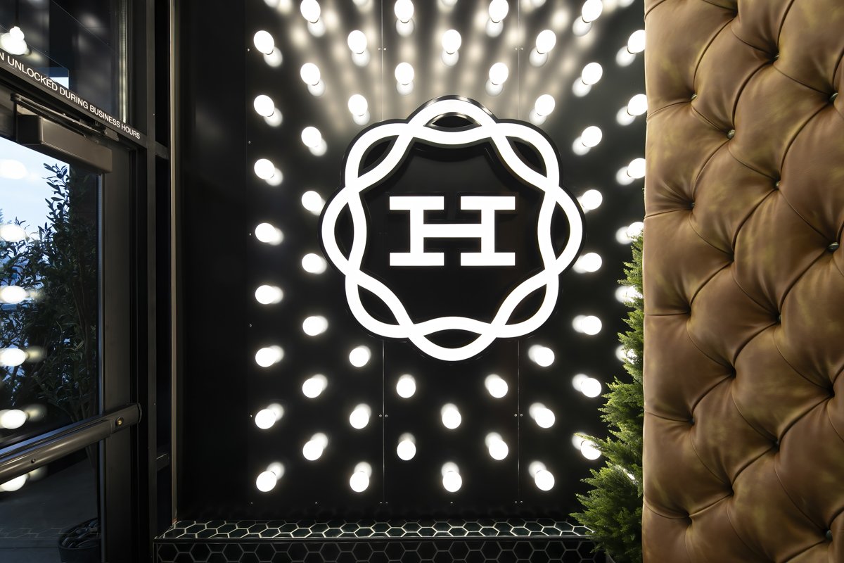 Decorative wall with illuminated bulbs surrounding a logo with a geometric design and the letter 'H' in the center, part of an upscale interior space.