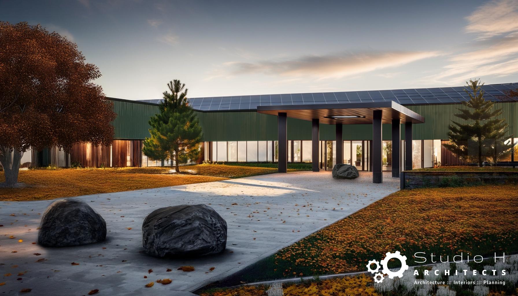 Modern architectural building with glass walls, a green roof with solar panels, and a covered entrance supported by black columns. The surrounding landscaping includes trees, rocks, and ground cover, with a pathway leading to the entrance.