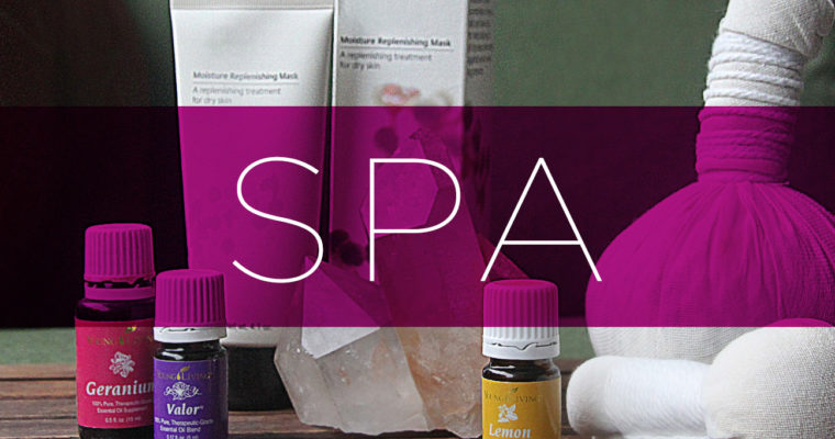 Spa setup with essential oils, a folded towel, and a herbal pouf on a wooden surface.