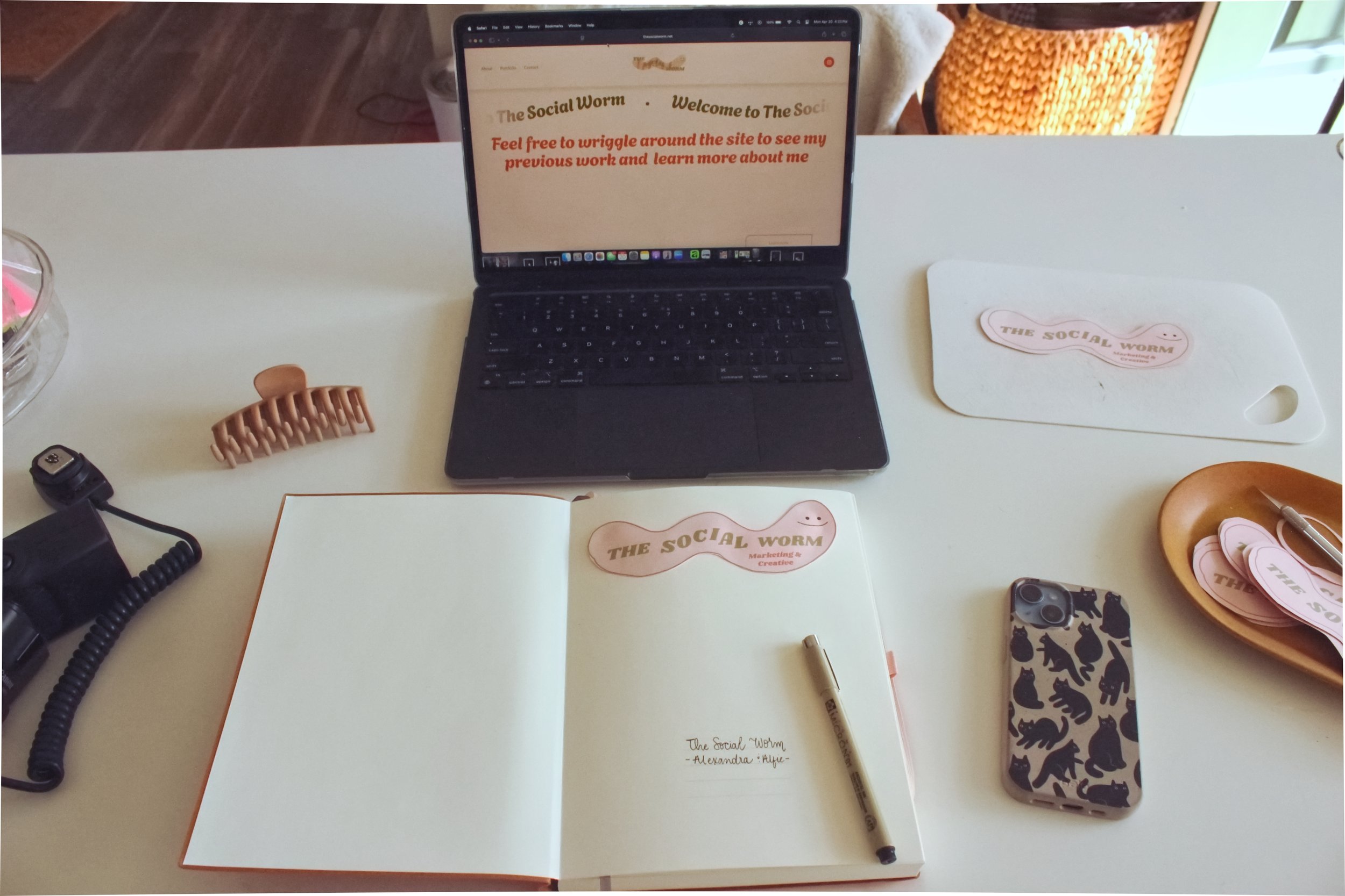 A notebook with the social worm business card taped on sitting on a desk with a laptop next to it with the webpage open.
