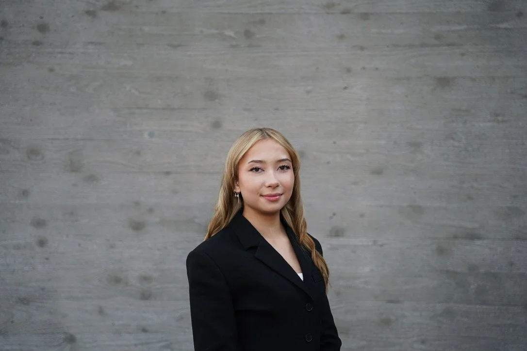 Professional portrait of a student standing on the University of Washington Bothell campus, with UWB flags visible in the background, photographed as a formal headshot.