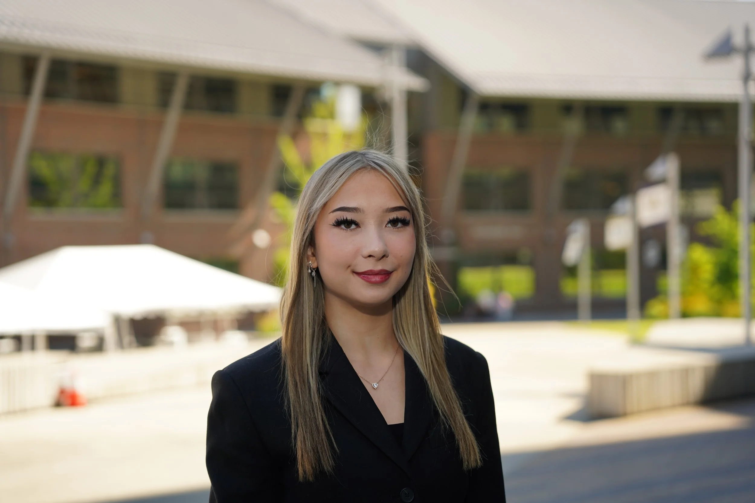 Professional portrait of a student standing on the University of Washington Bothell campus, with UWB flags visible in the background, photographed as a formal headshot.