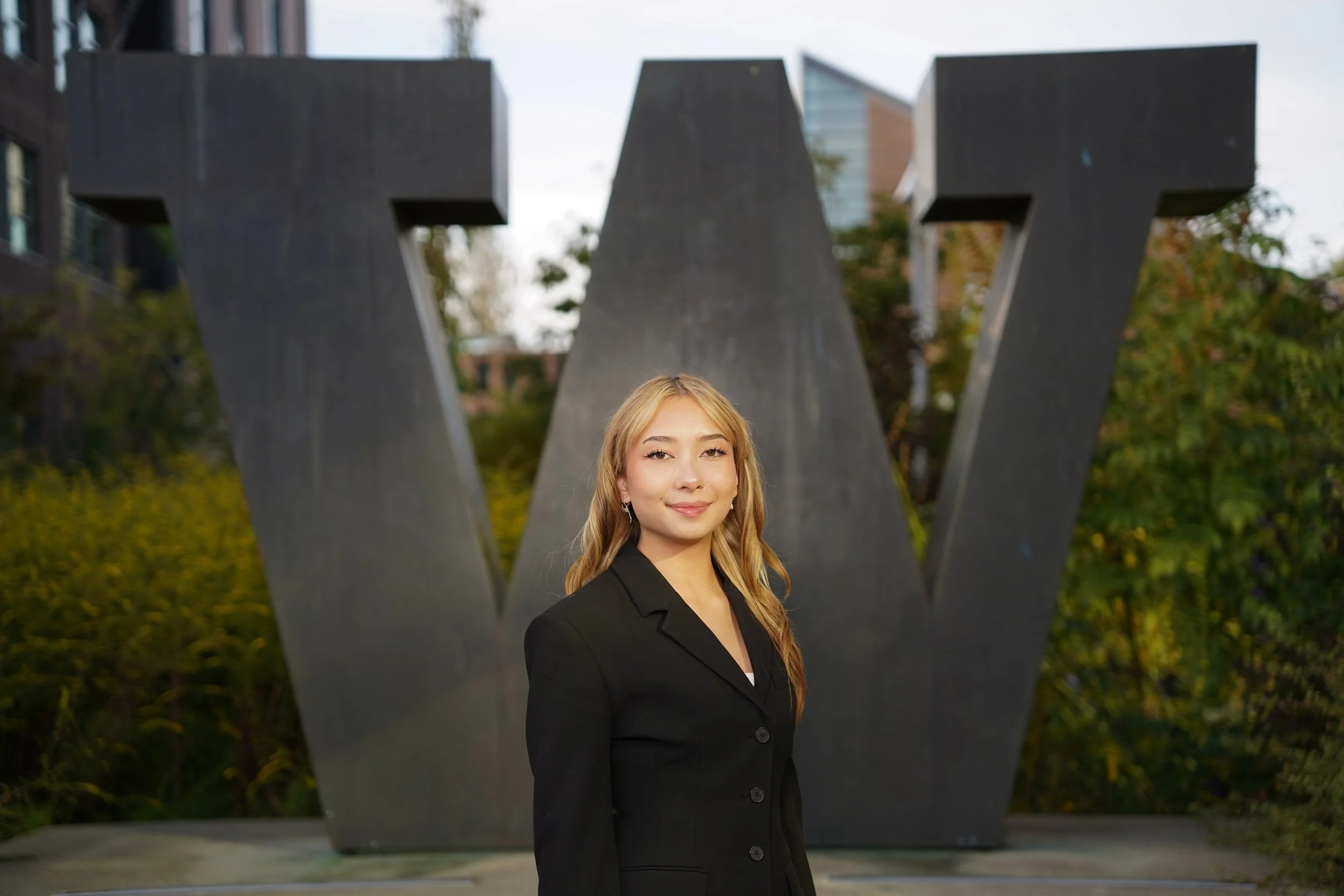 Professional portrait of a student standing on the University of Washington Bothell campus, with UWB flags visible in the background, photographed as a formal headshot.